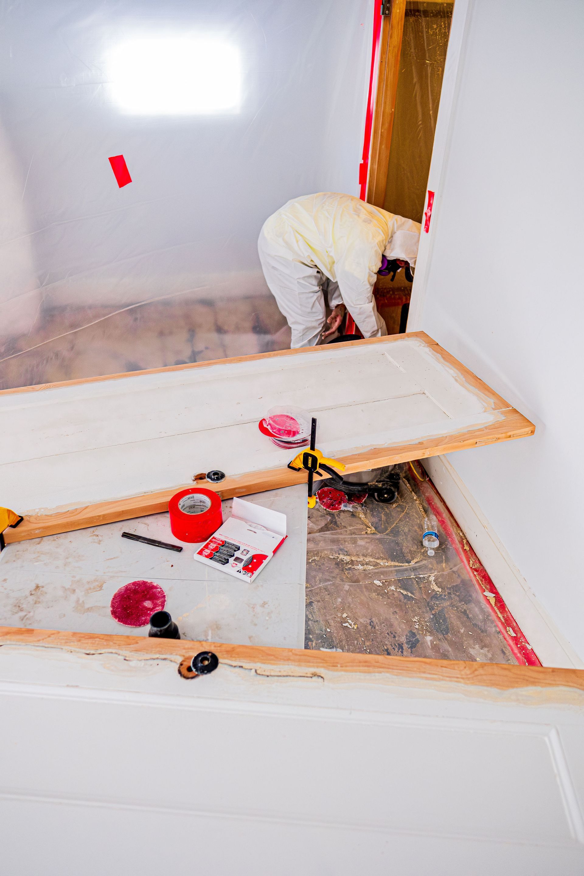Person installing flooring in a room with tools and wood planks scattered on the floor.