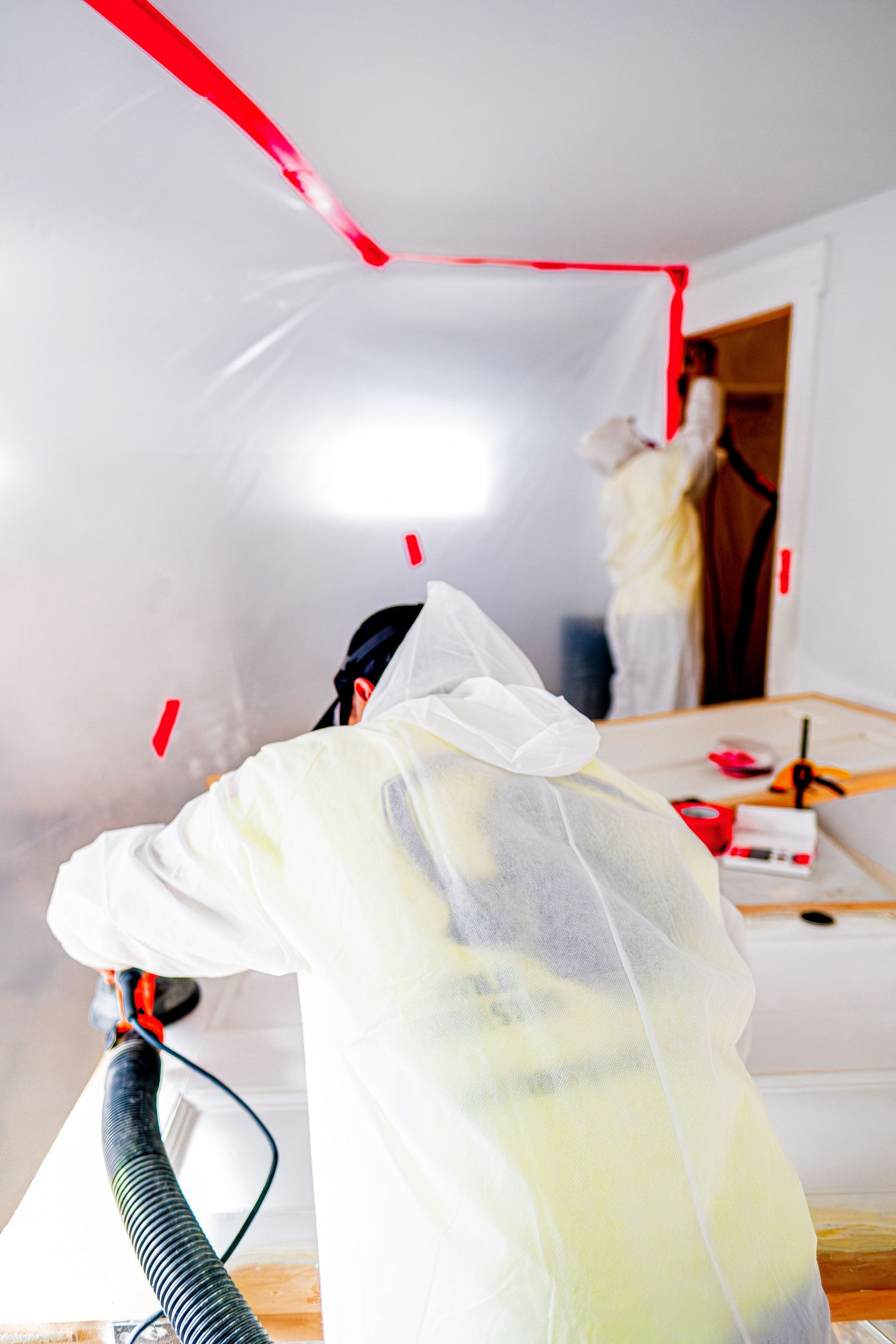 People painting a room ceiling and trim, with red tape and protective coverings in place