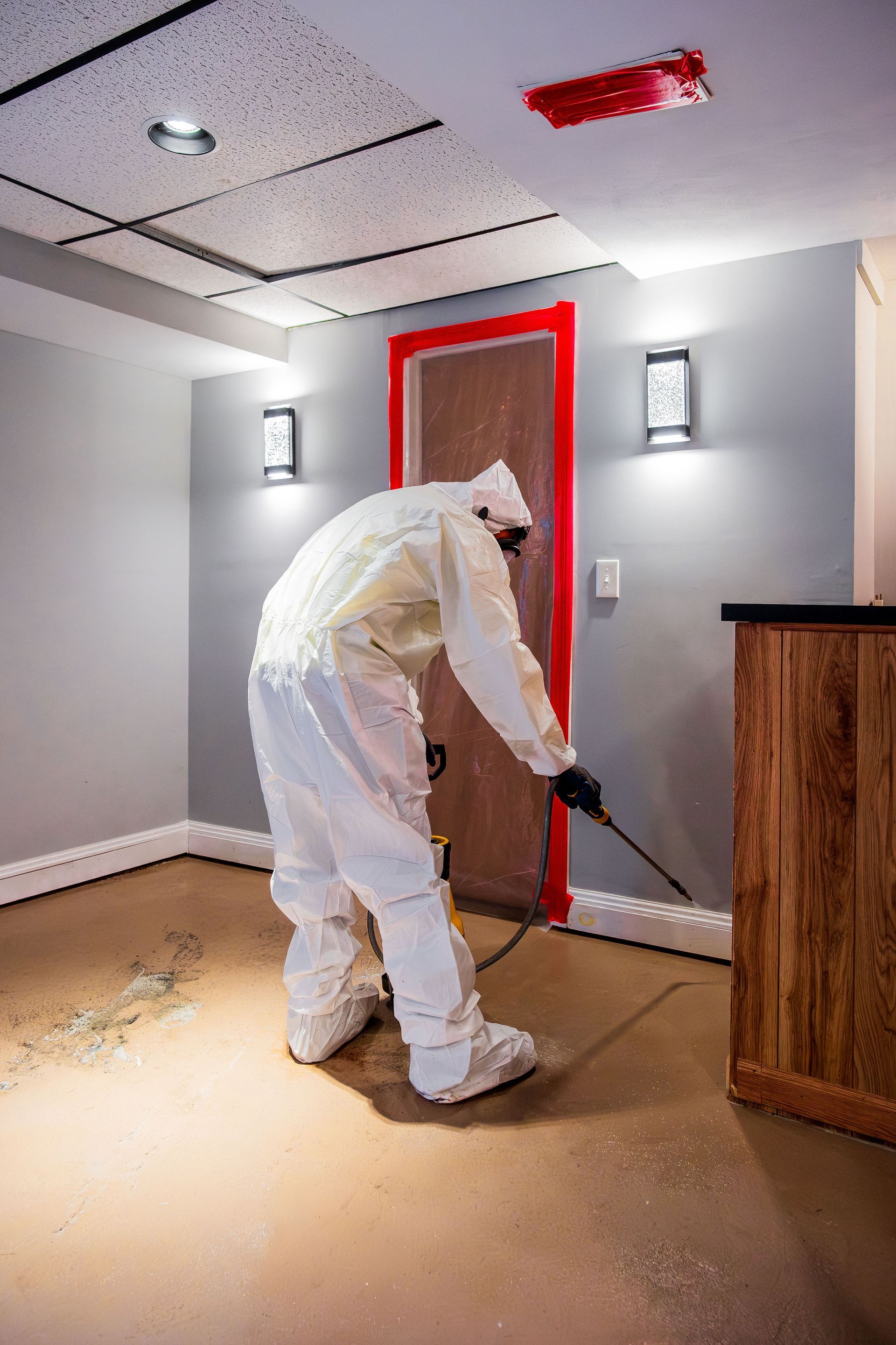 Worker in white protective suit painting around a red-framed door in a room under renovation.