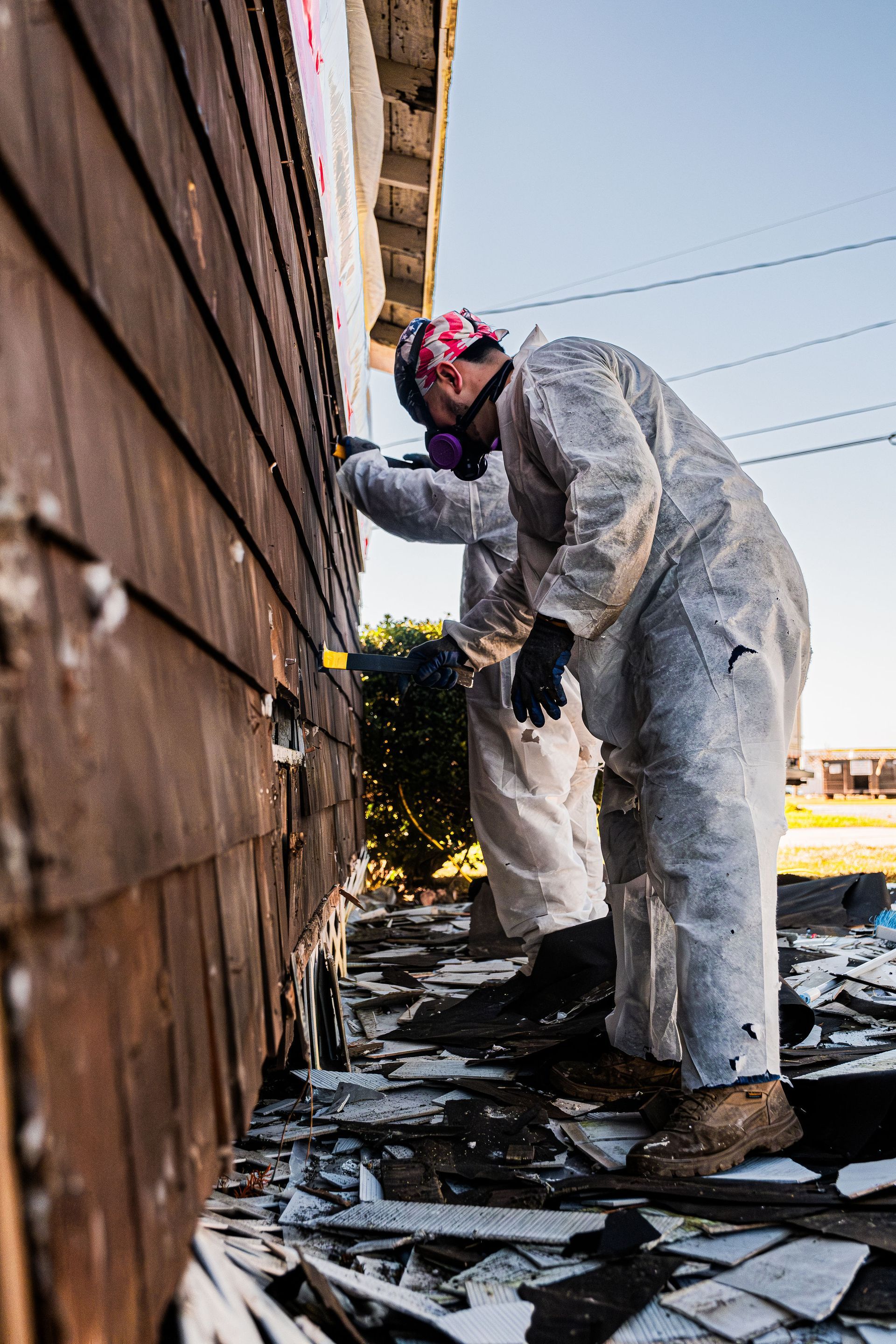 Worker in white protective suit removing siding from a weathered wall outdoors