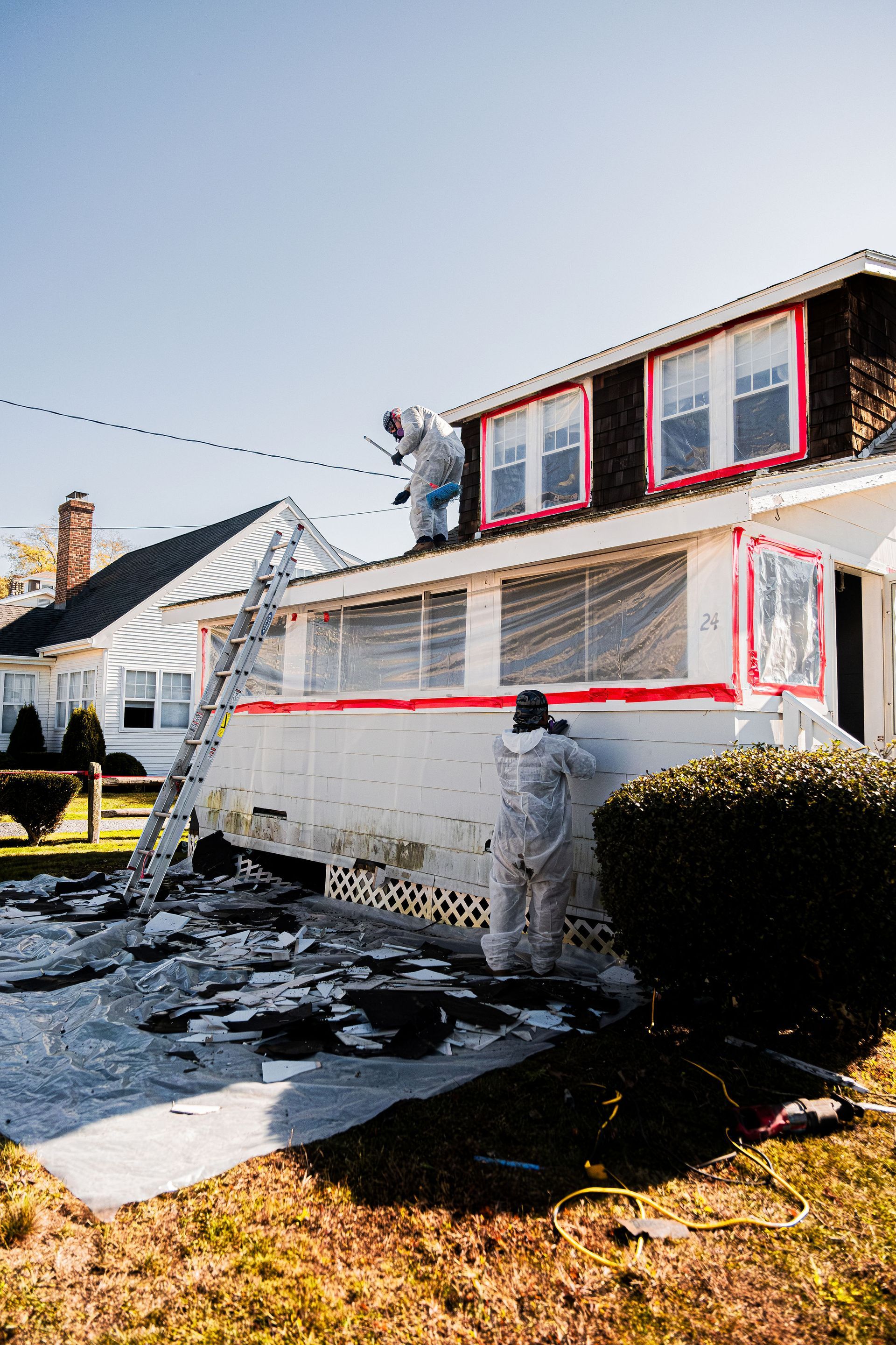 House exterior with red-trimmed windows, snow on the ground, and a person working near the wall