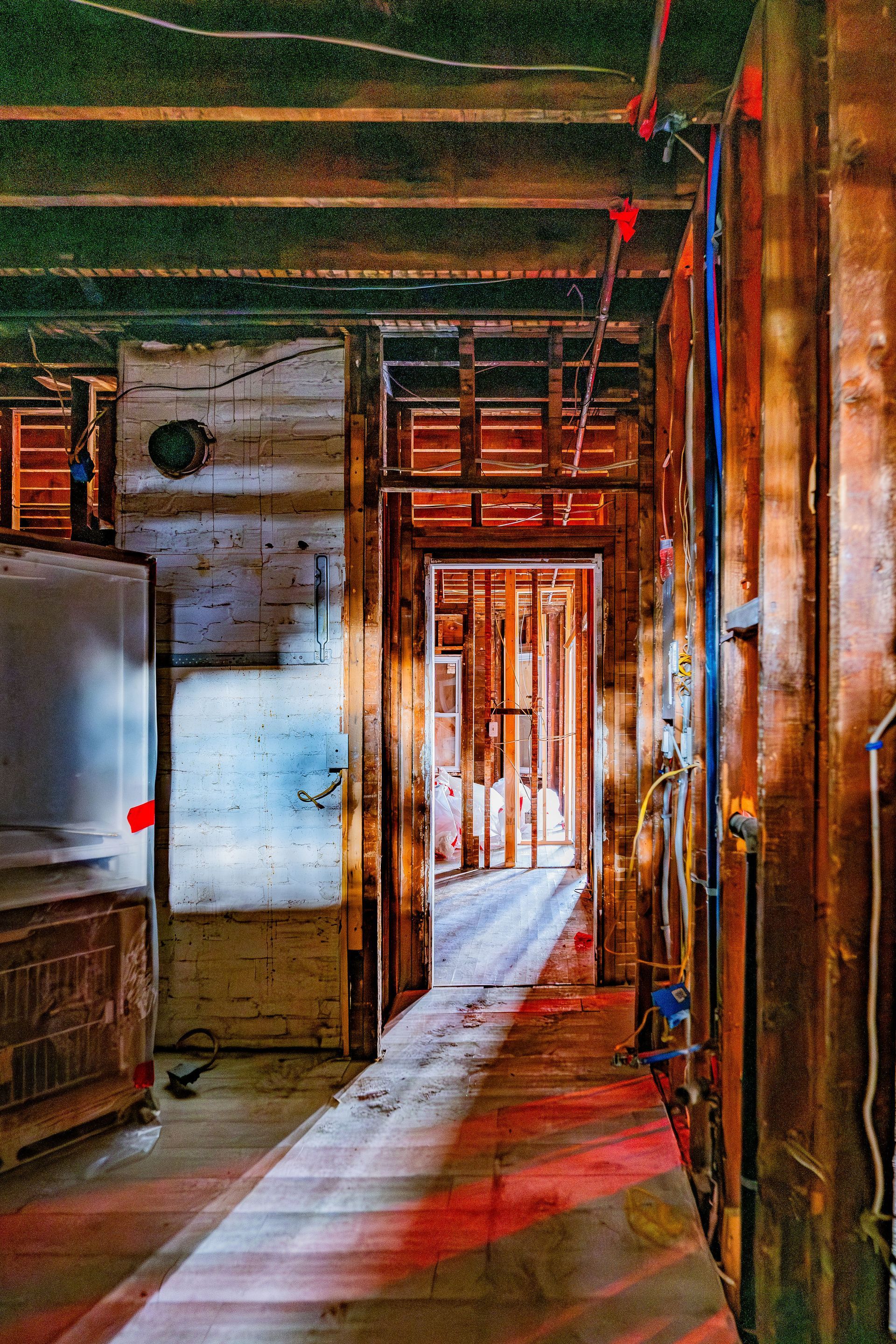 Narrow industrial hallway with peeling walls, pipes, and sunlight streaming through an open doorway