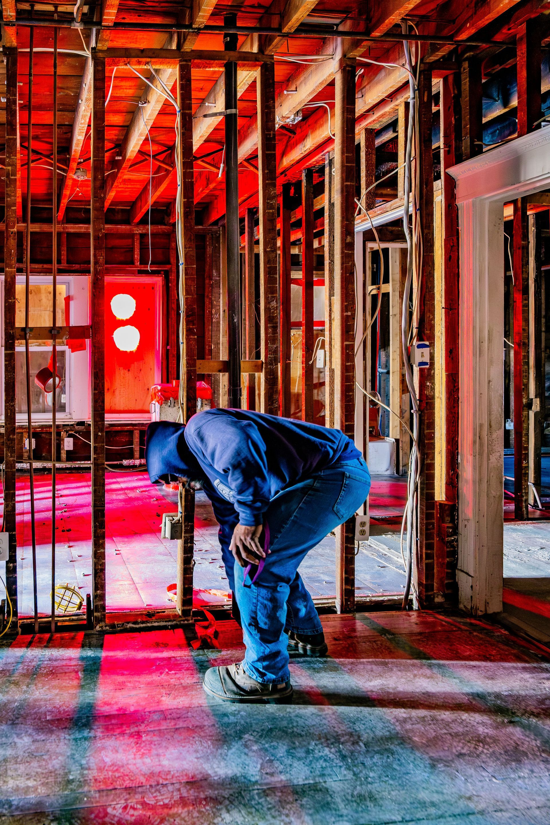 Person bending over inside an unfinished building with exposed wooden framing and red lighting.