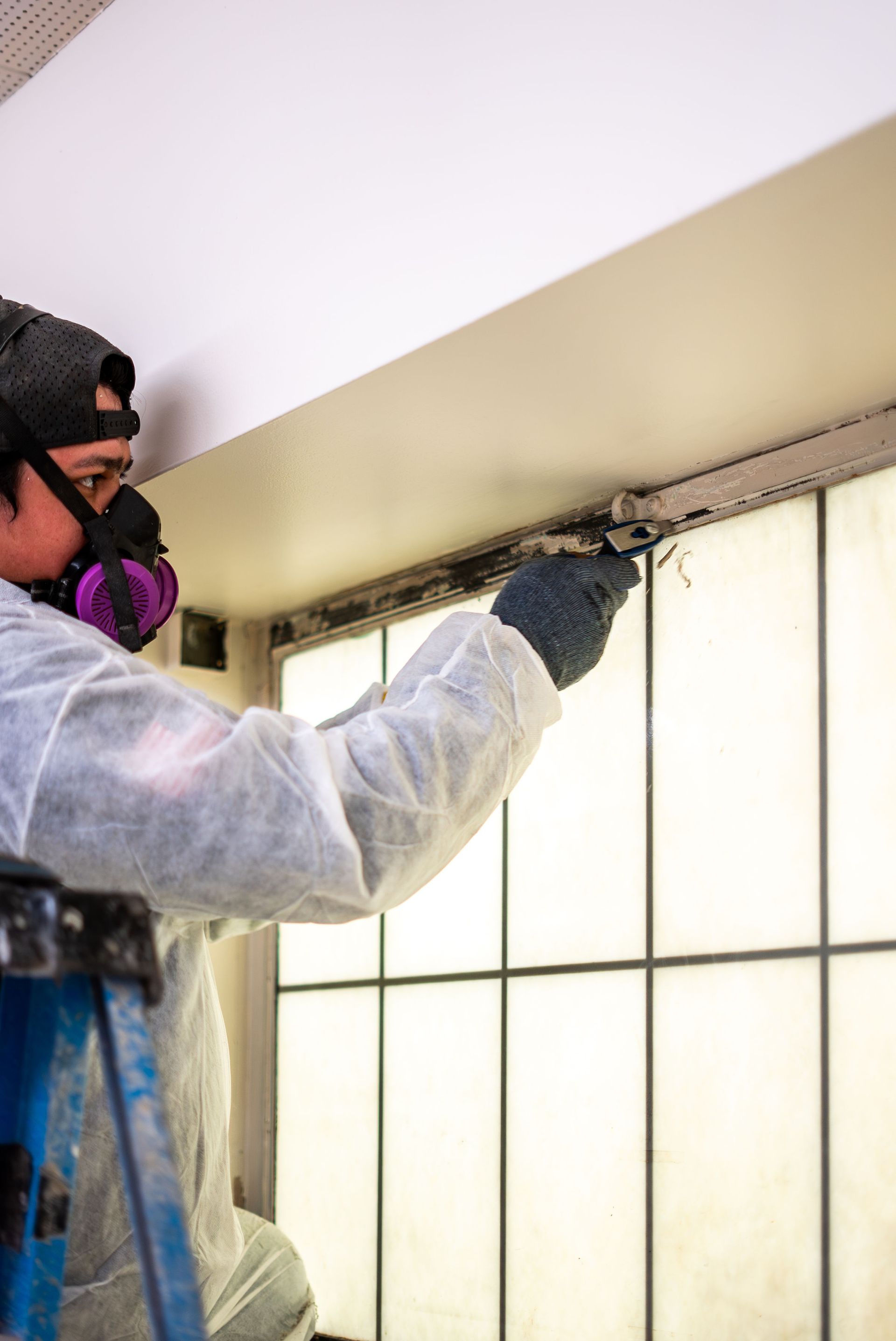 Worker wearing a respirator spray-painting a window frame near a ceiling