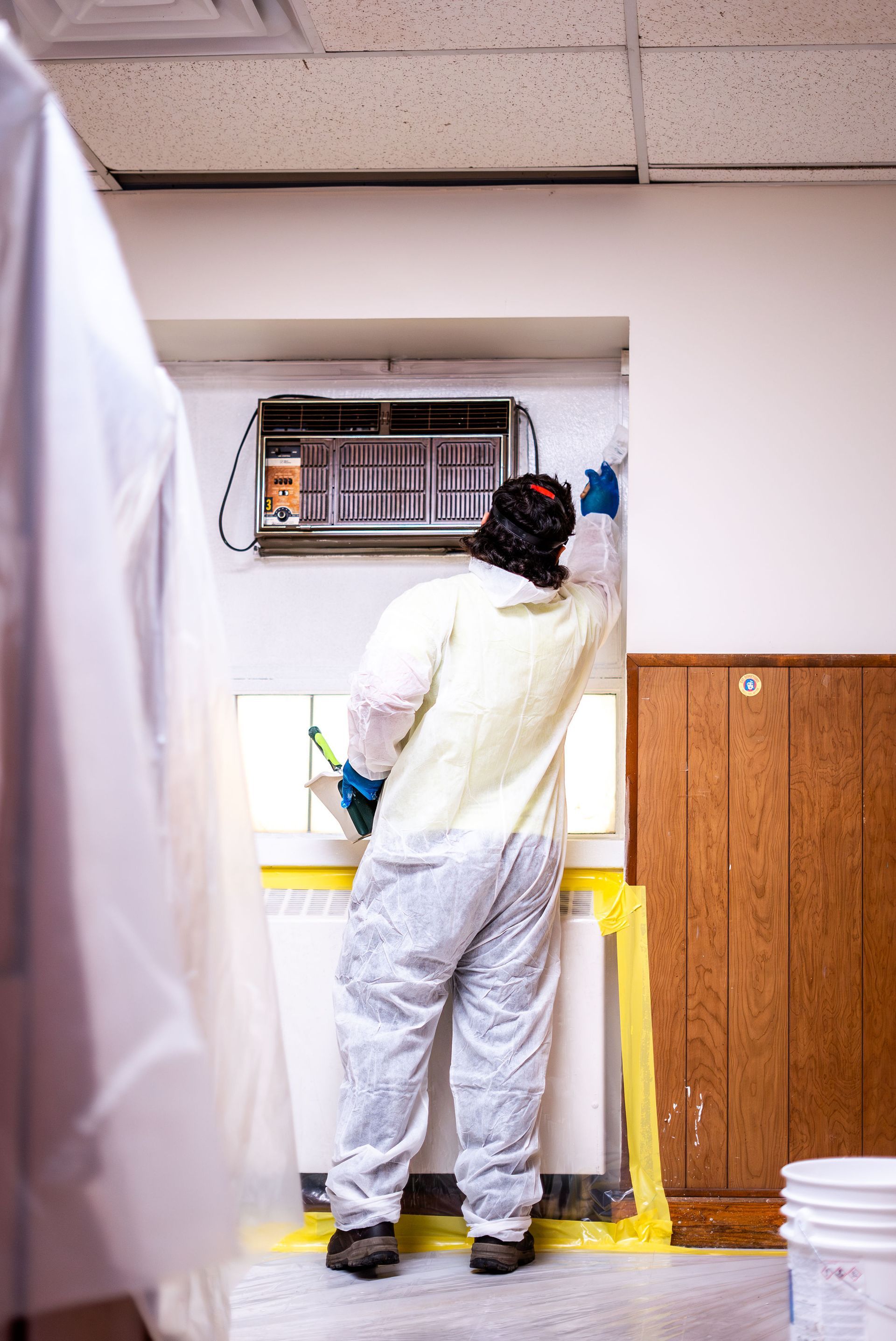 Person in a white coat working at an open wall-mounted electrical panel in a utility room.