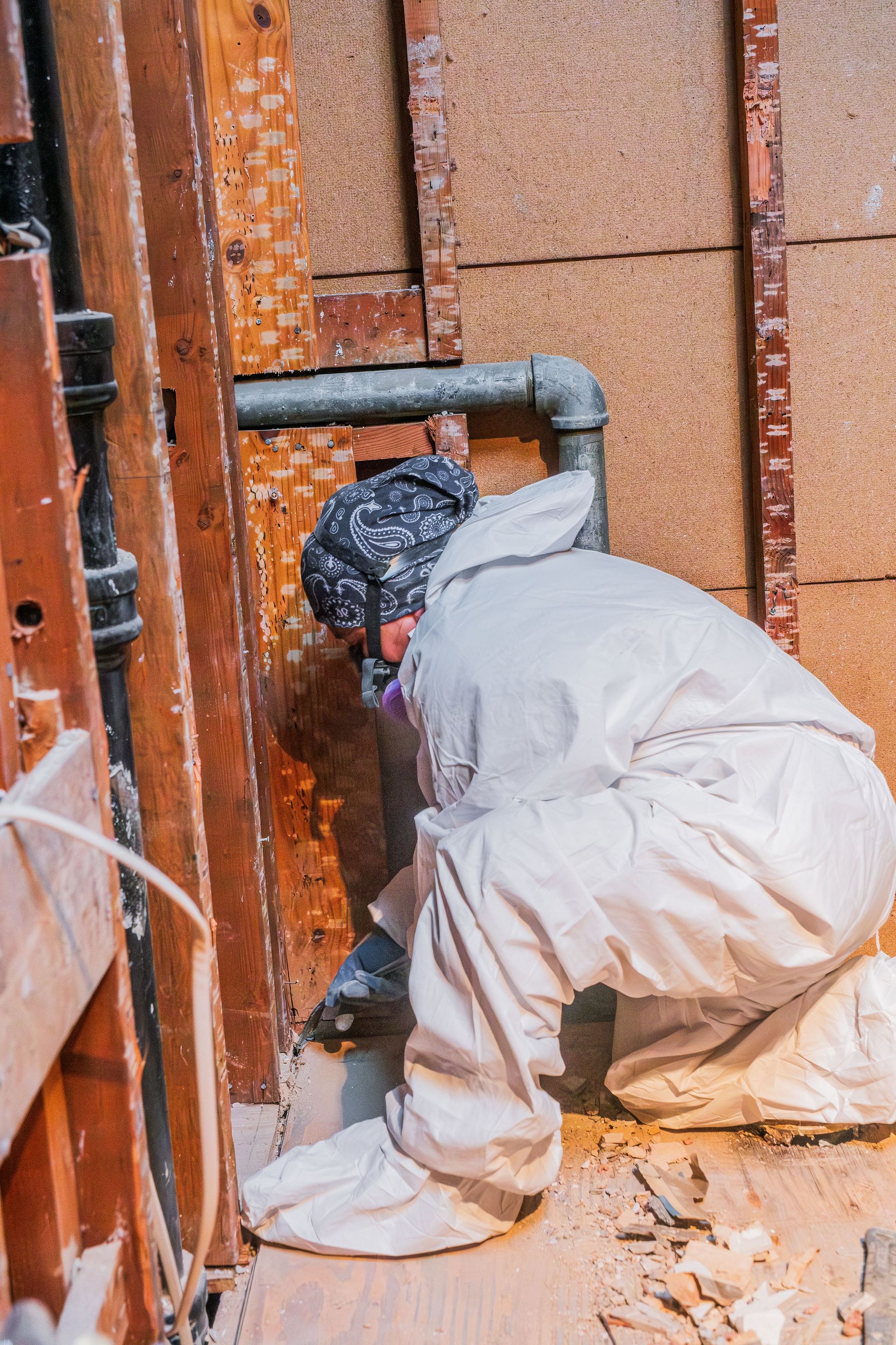 Worker in white coveralls crouches beside exposed pipes during construction.