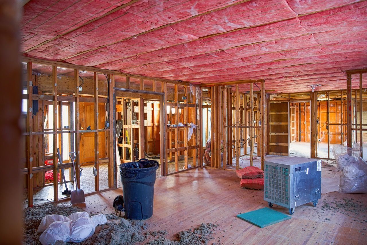 An interior view of a room under construction, with exposed wooden wall studs and pink insulation installed on the ceiling.