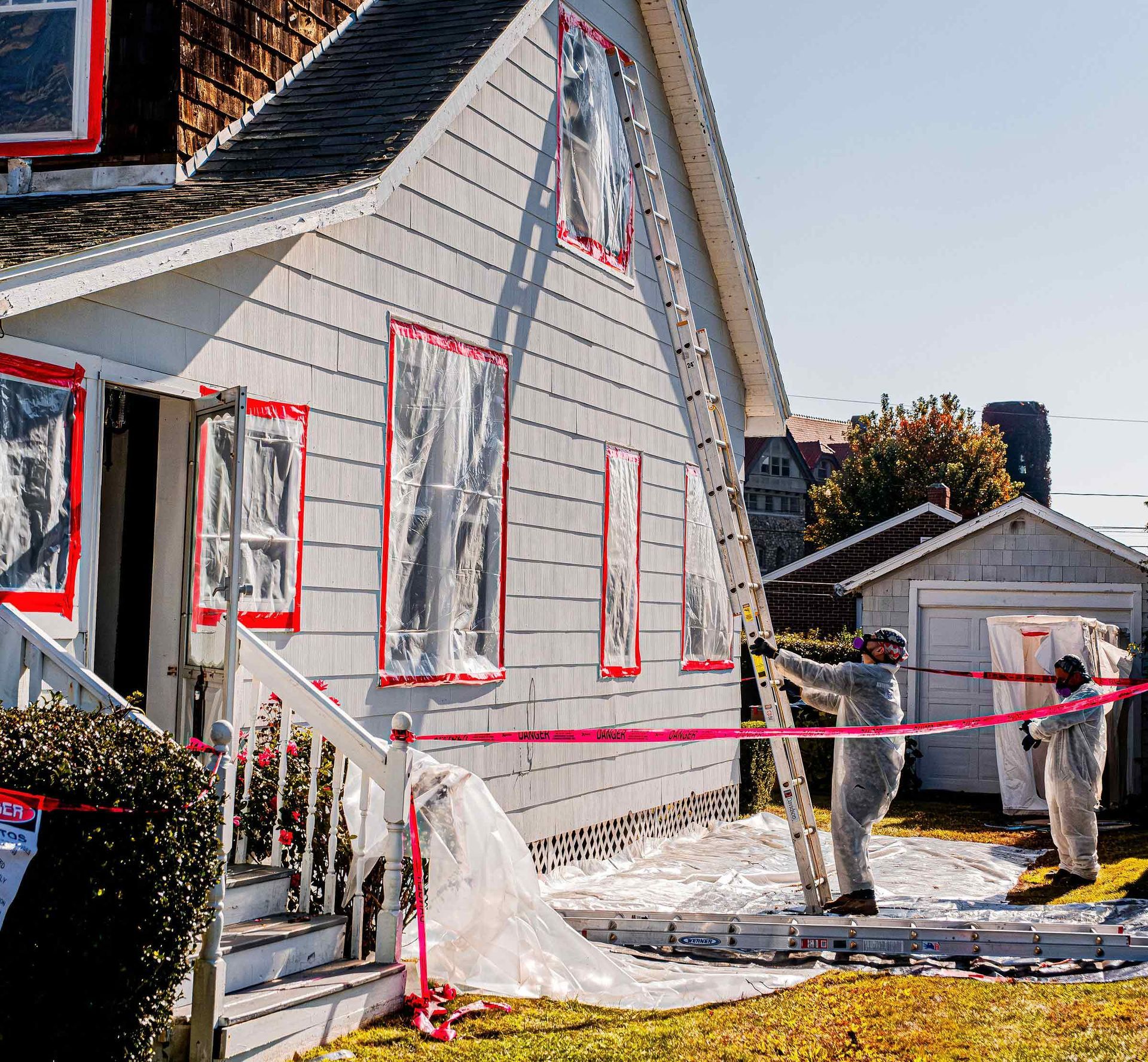 House exterior under renovation with red masking tape and plastic sheeting; person standing by the garage