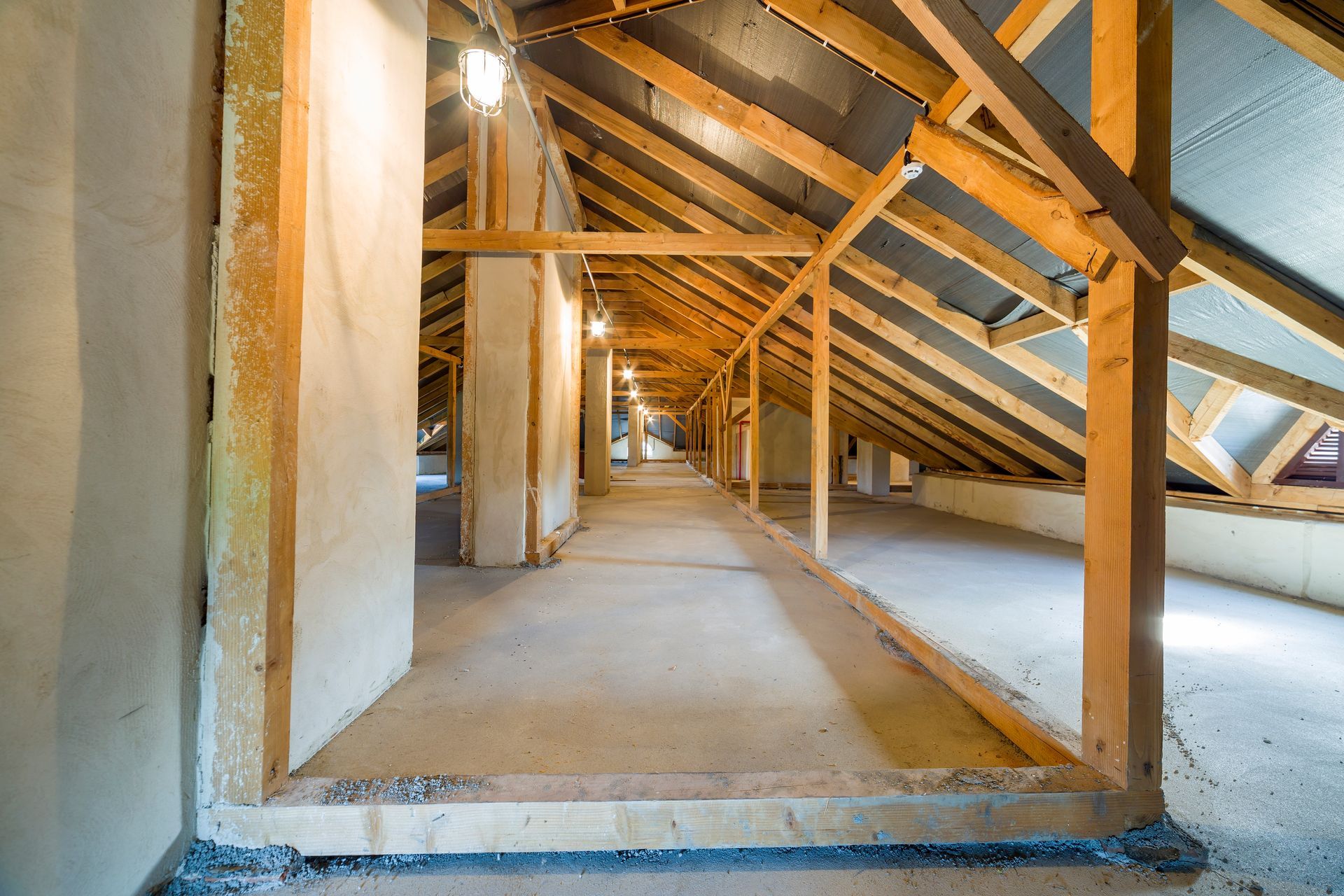 Attic interior with exposed wooden beams, insulation, and unfinished drywall framing a long walkway