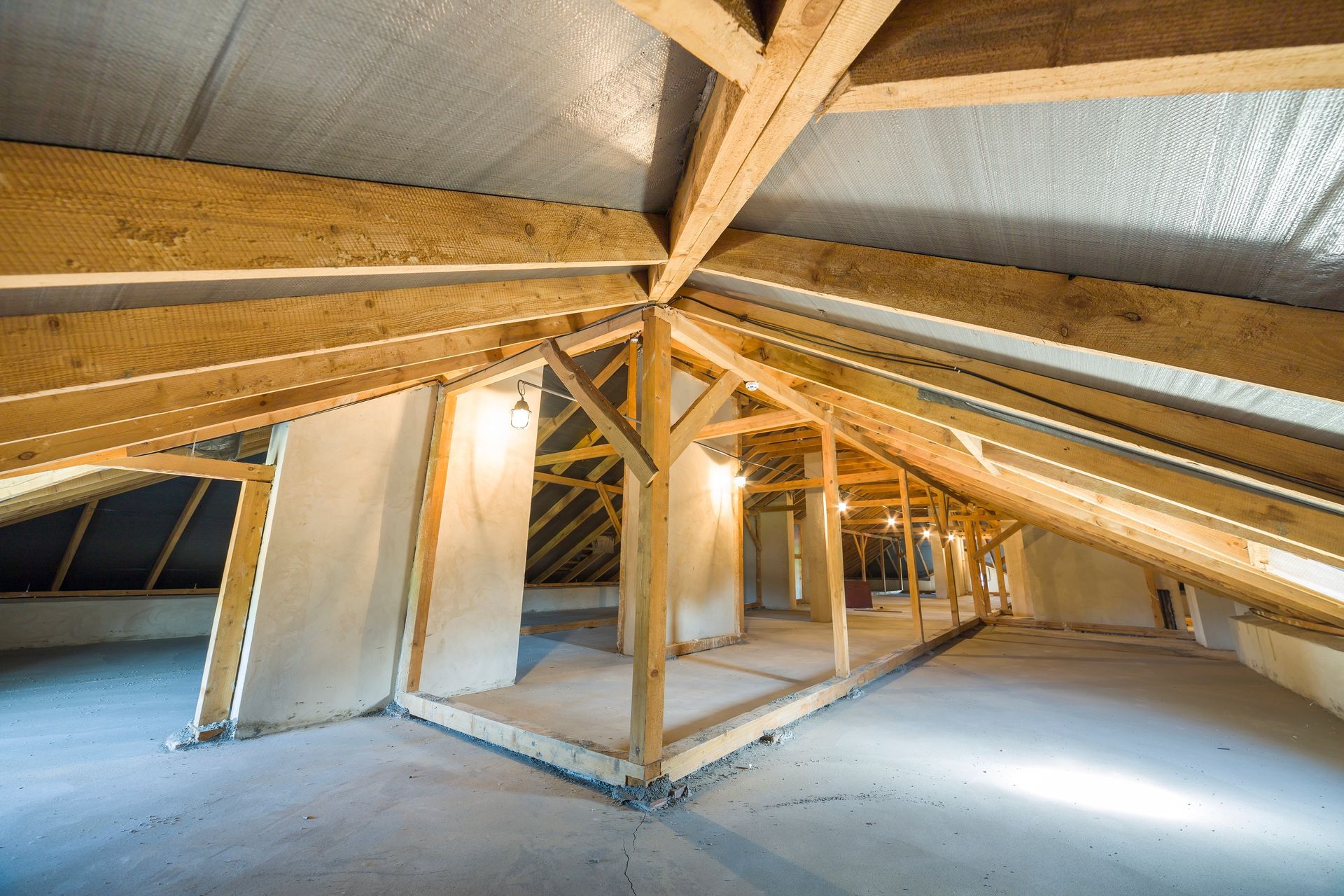 Interior of an unfinished attic with exposed wooden beams, insulation, and a concrete floor