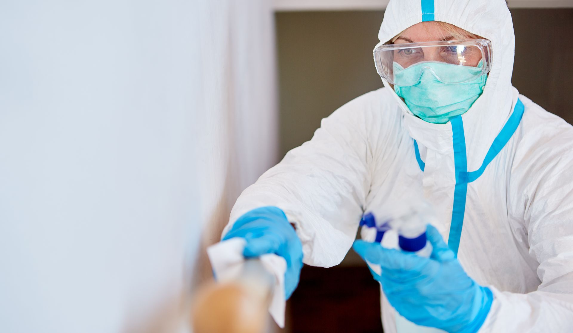 Healthcare worker in white protective gear, mask, and gloves reaching toward a patient in a clinical setting