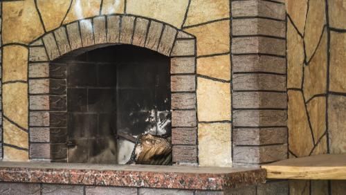 Rustic stone fireplace with dark firebox, showing ash remnants from recent use, built in a natural stone setting.
