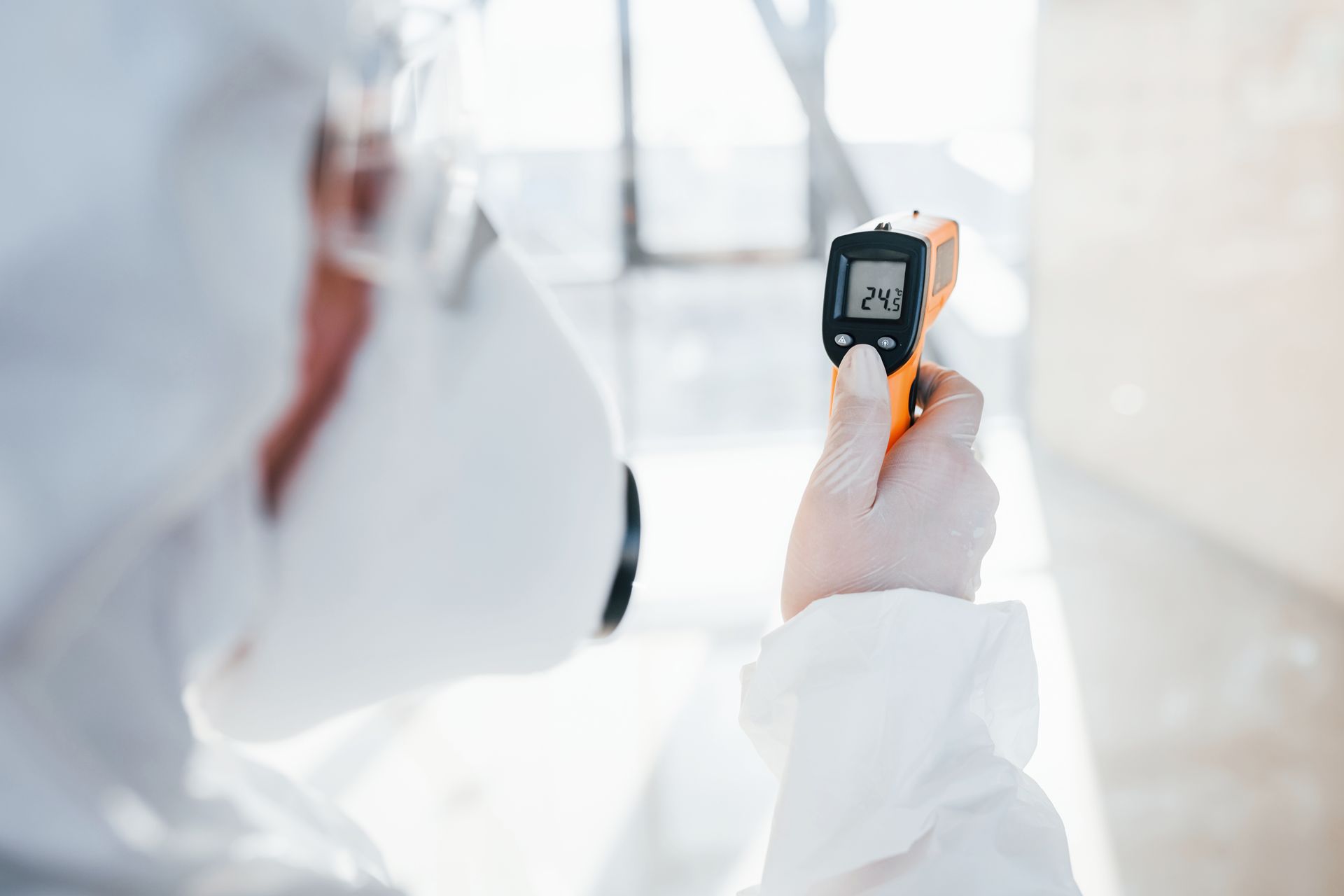 Person in protective gear using a handheld infrared thermometer in a bright lab or clinical setting