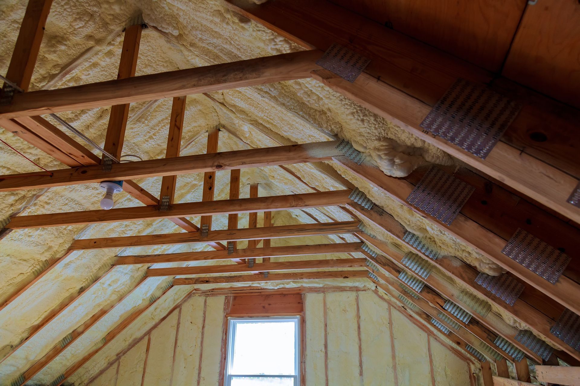 Interior of an attic with exposed wooden rafters and insulation, centered on a small window.