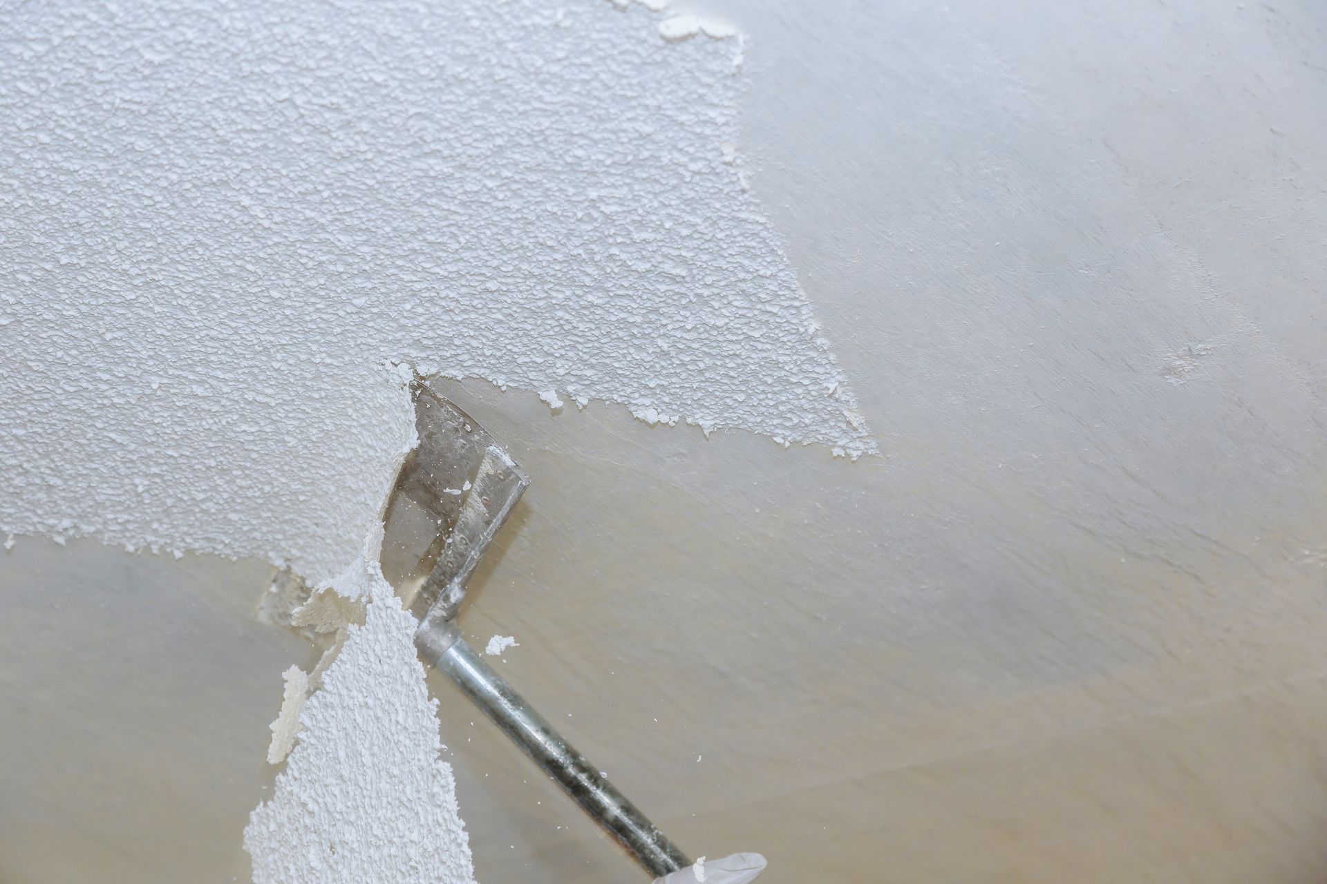 A paint scraper peeling white paint from a textured wall during renovation