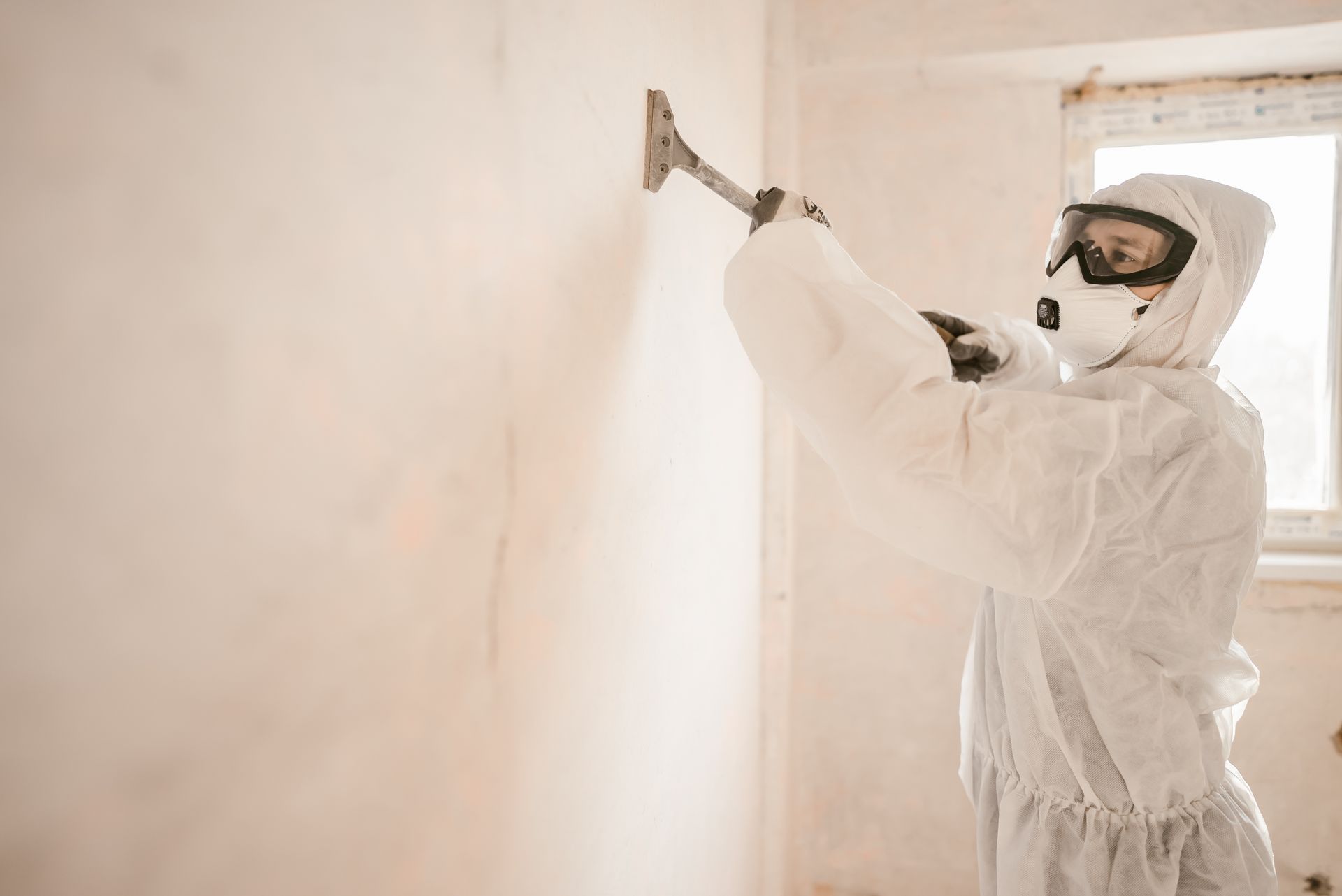 Person in protective gear painting a wall with a roller in a light-colored room