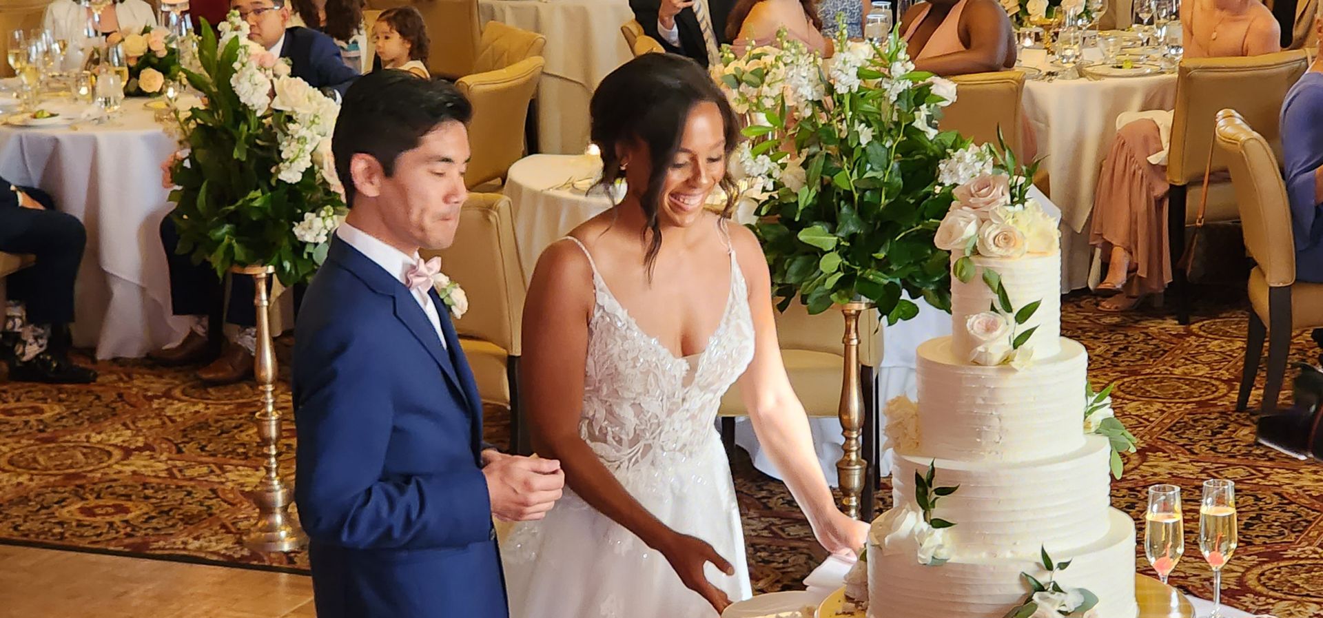 A bride and groom are cutting their wedding cake in front of their wedding guests.