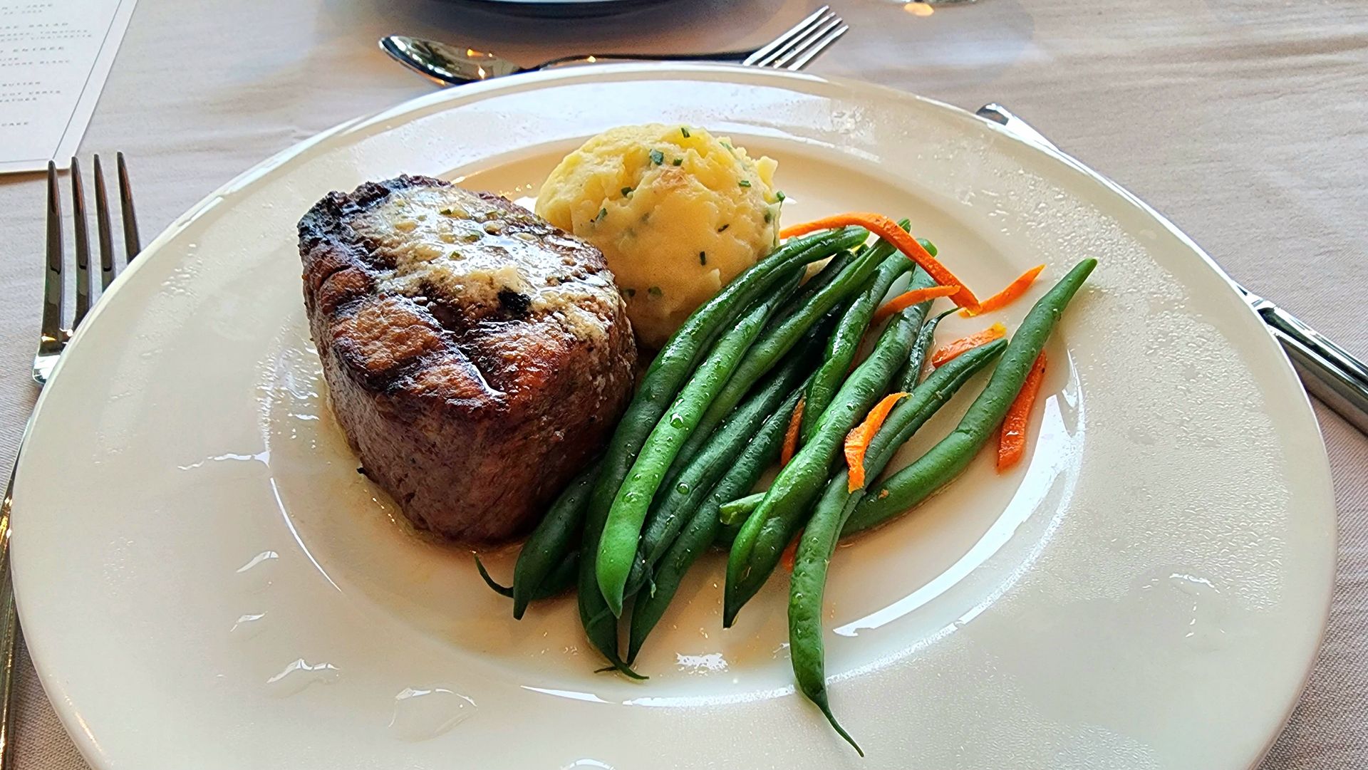 A white plate topped with a steak , green beans , mashed potatoes and carrots.