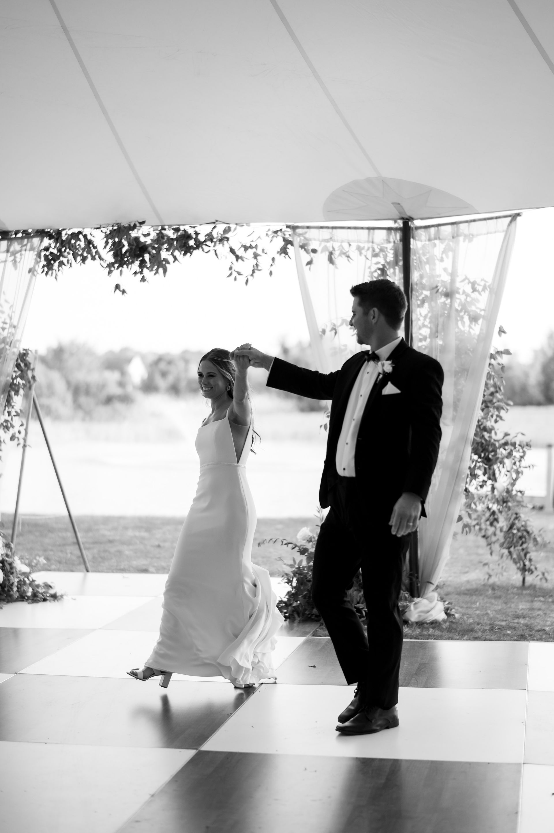 A black and white photo of a bride and groom dancing under a tent.