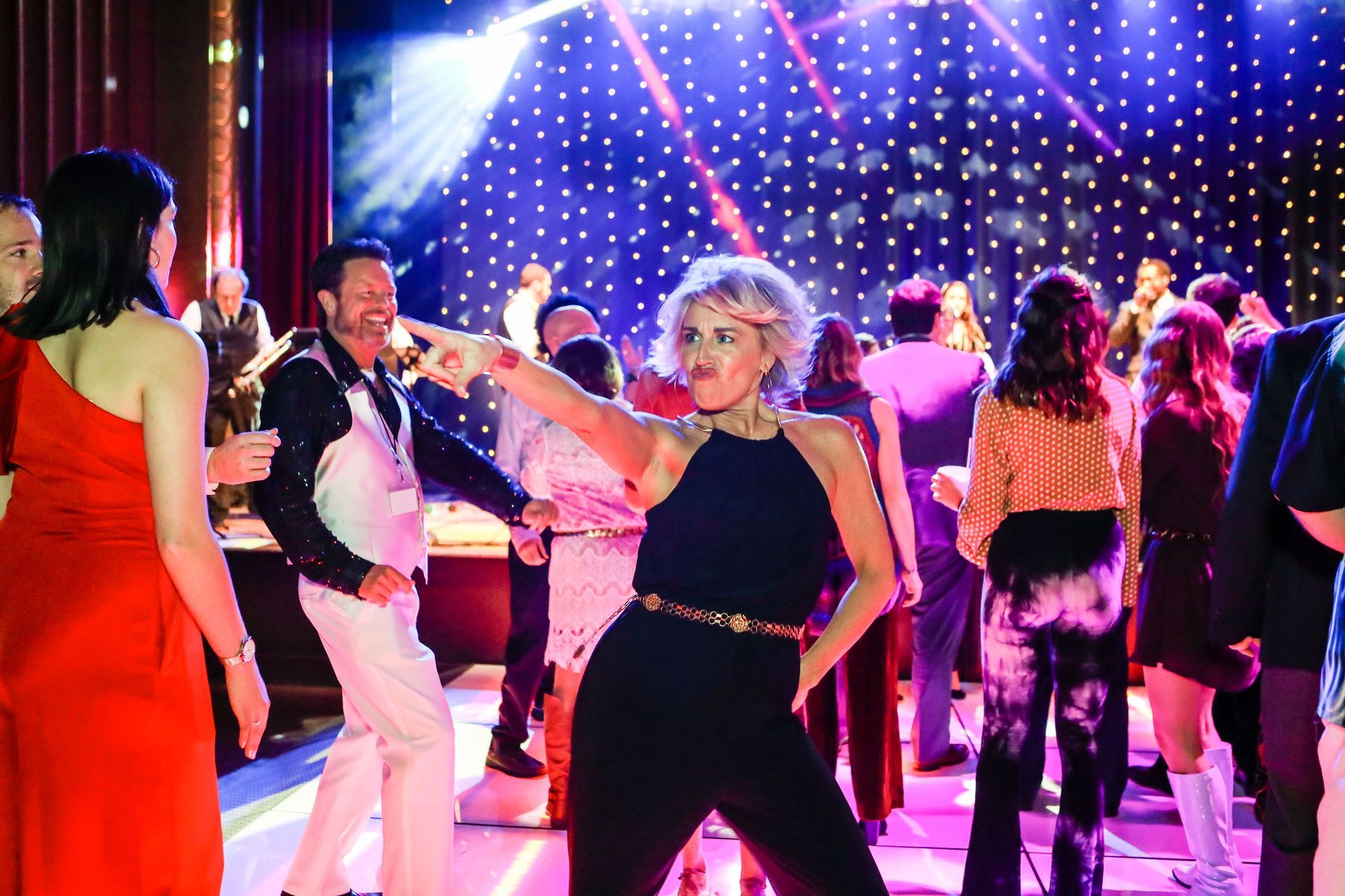 a woman in a black jumpsuit is dancing in a crowd of people at a party .