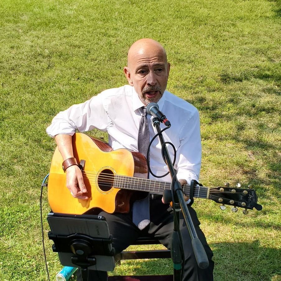a man with Mainstreet Soul is sitting on a stool playing an acoustic guitar and singing into a microphone.
