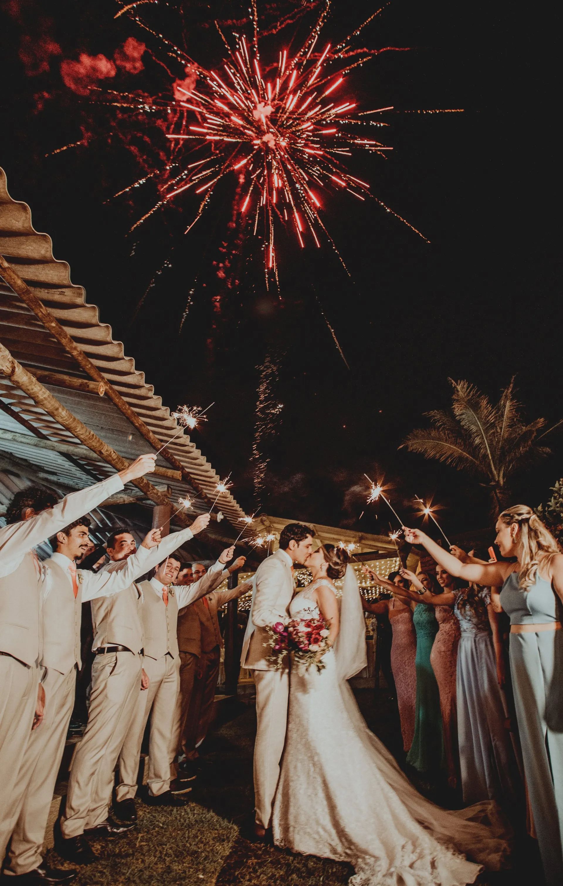 a bride and groom kiss in front of a fireworks display