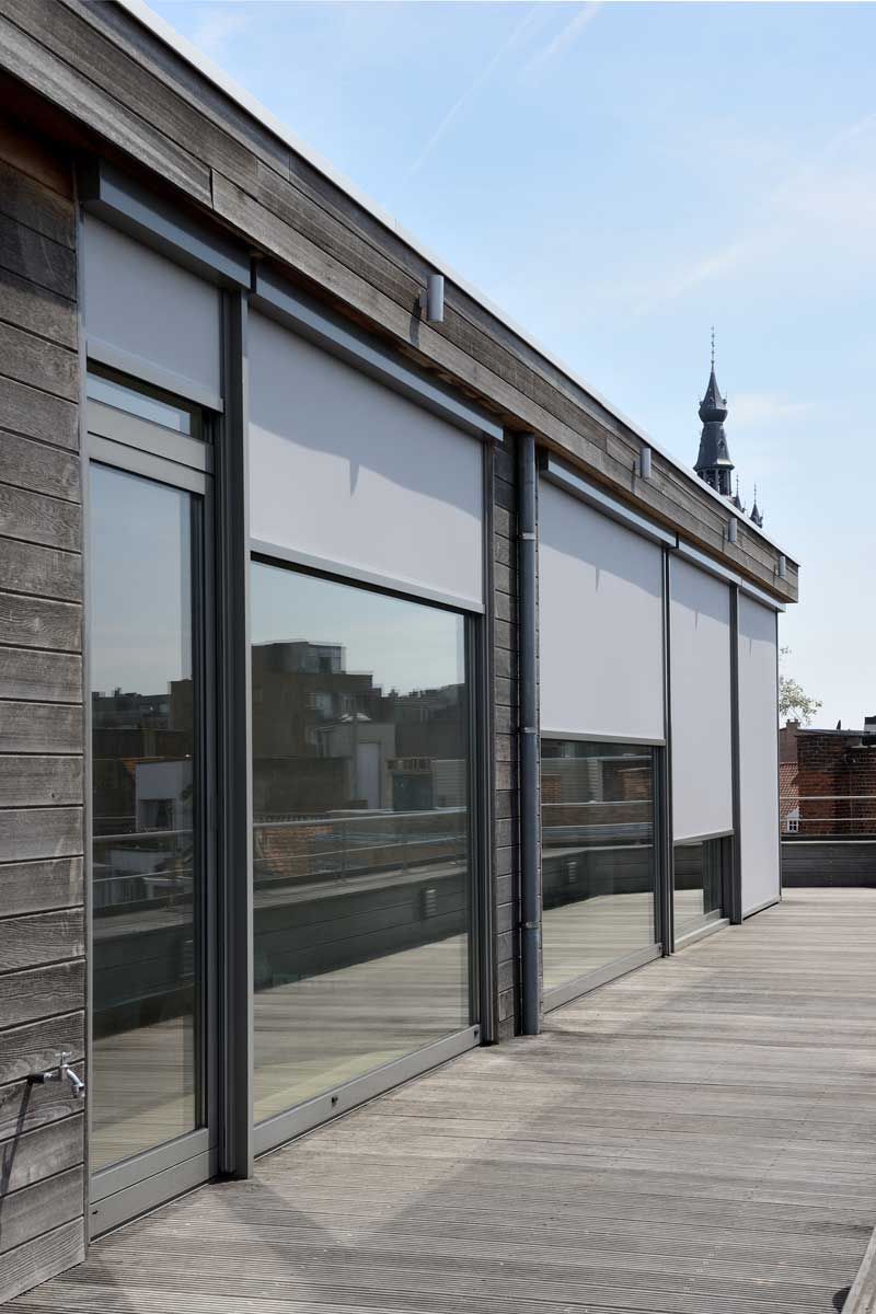 Moderne tagterrasse med glasdøre, reflekterende vinduer og et fjernt kirkespir under en blå himmel
