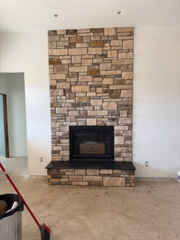 Living room fireplace with stacked stone surround and black hearth on a white wall