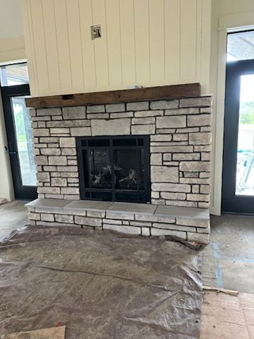 Stone fireplace with black insert in a room under renovation, surrounded by protective floor covering.