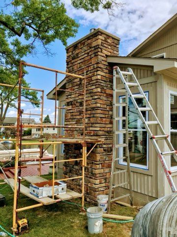 Construction scaffolding around a stone chimney beside a house under repair