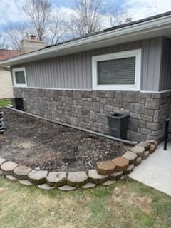 House exterior with stone veneer, window, and curved border edging a bare garden bed