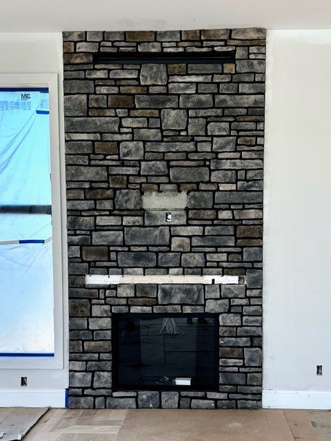 Stone fireplace with black firebox centered on a white wall, flanked by a window on the left.