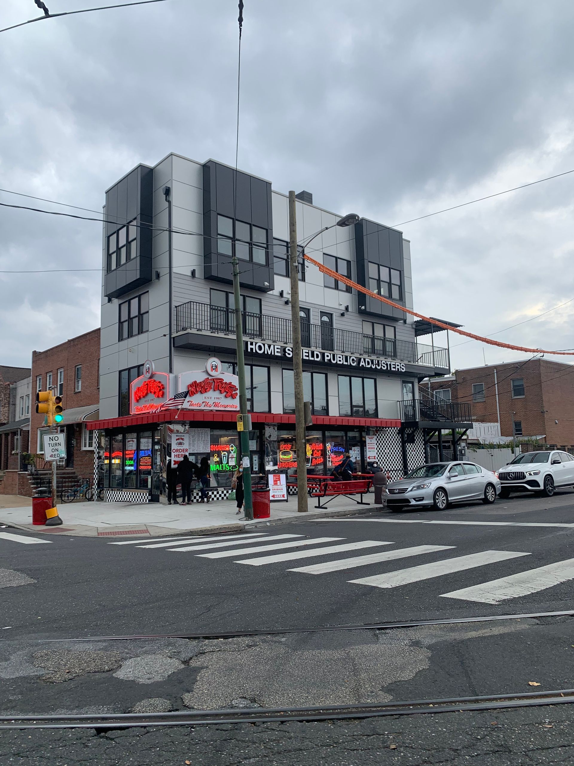 A multi-story building on a city corner with a ground-floor retail shop, storefront signs, and a crosswalk nearby.
