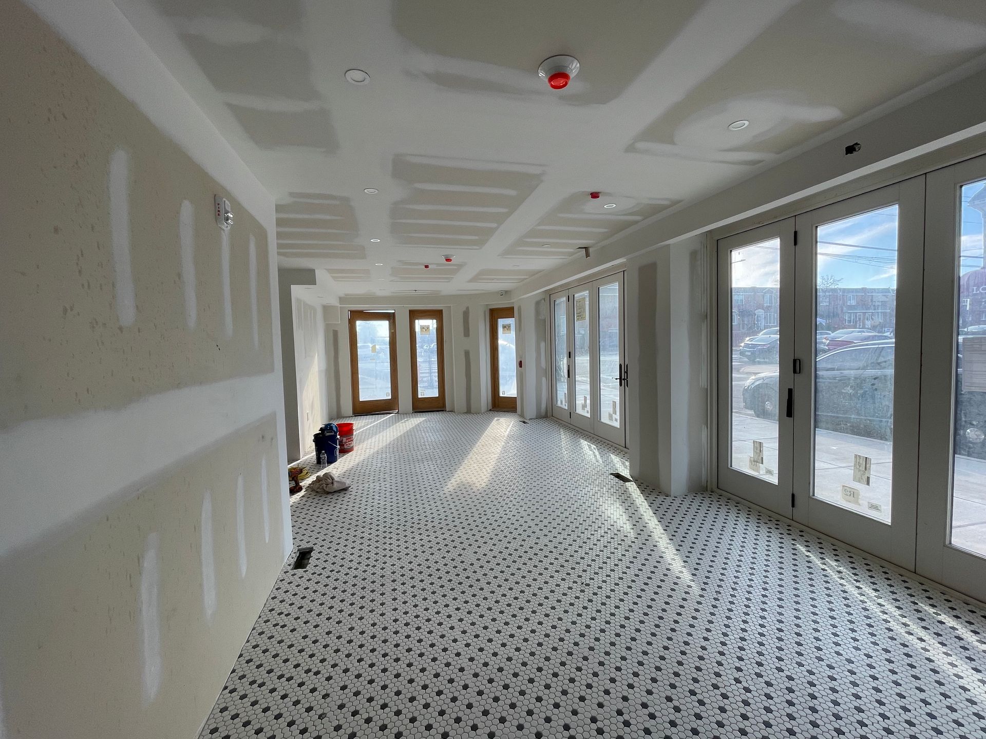 An unfinished room with newly installed drywall, a tiled floor with a geometric pattern, and floor-to-ceiling glass doors.