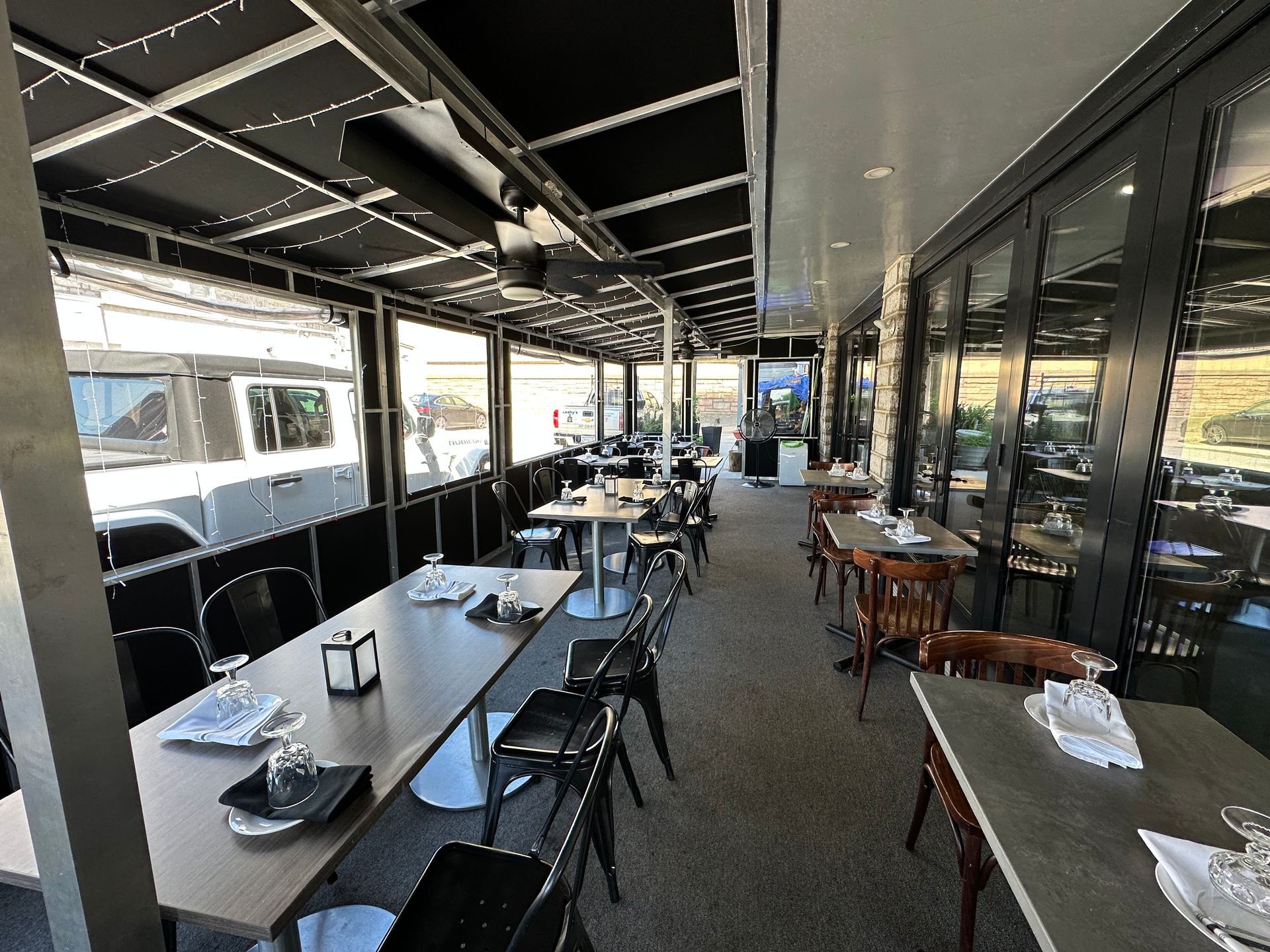 An outdoor restaurant patio with multiple tables and chairs arranged along a covered, partitioned deck.
