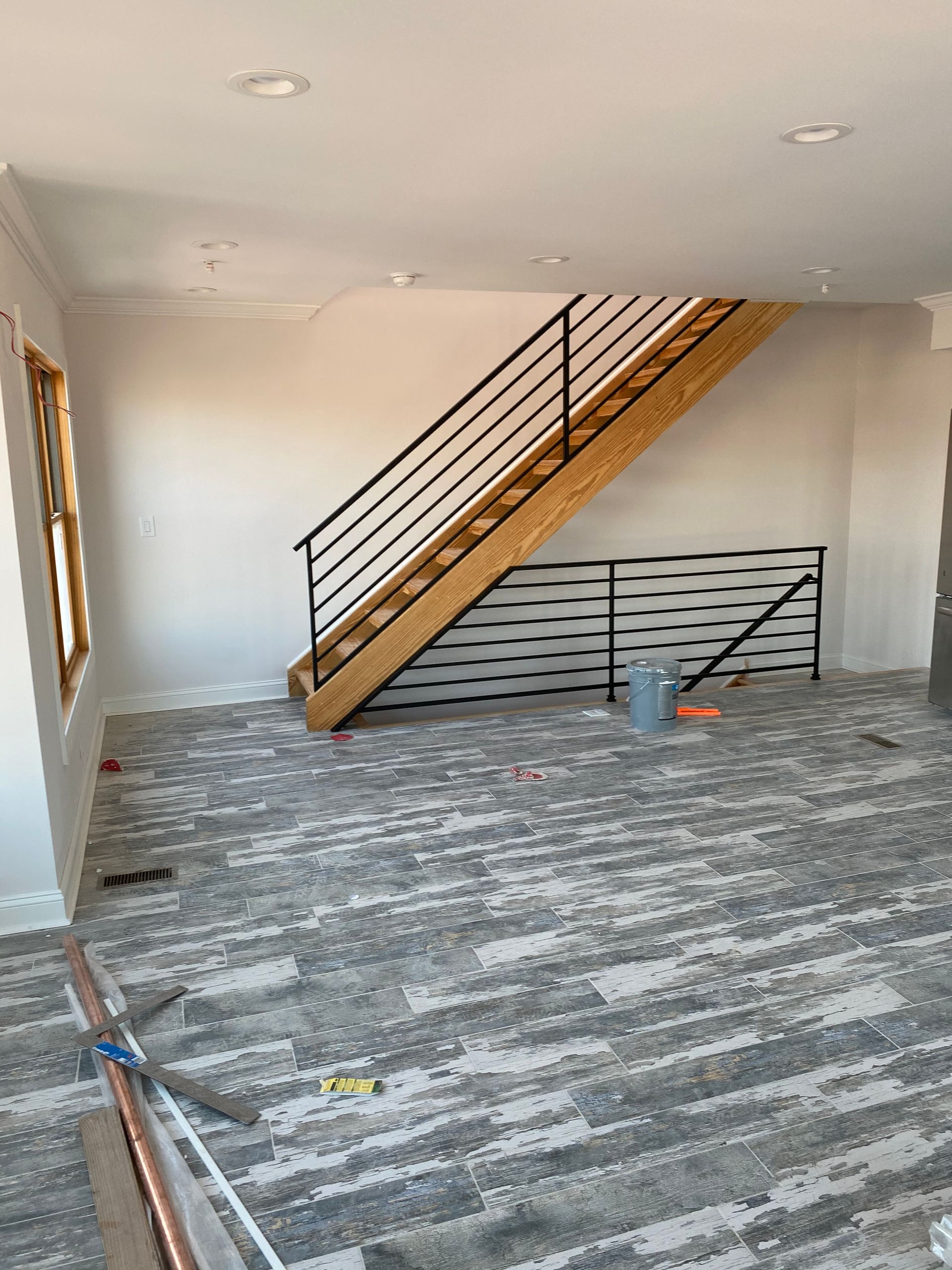 A wooden staircase with a black metal railing stands in a room with light-colored walls and patterned gray carpet flooring.