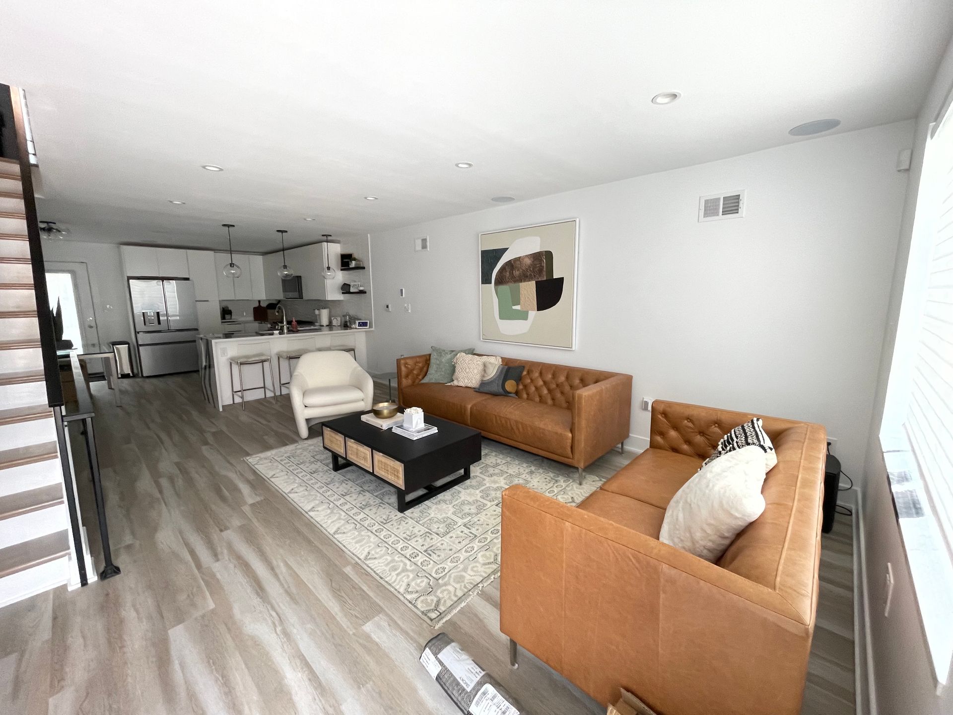 A modern living room with two brown leather tufted sofas, a coffee table, and an open kitchen in the background.