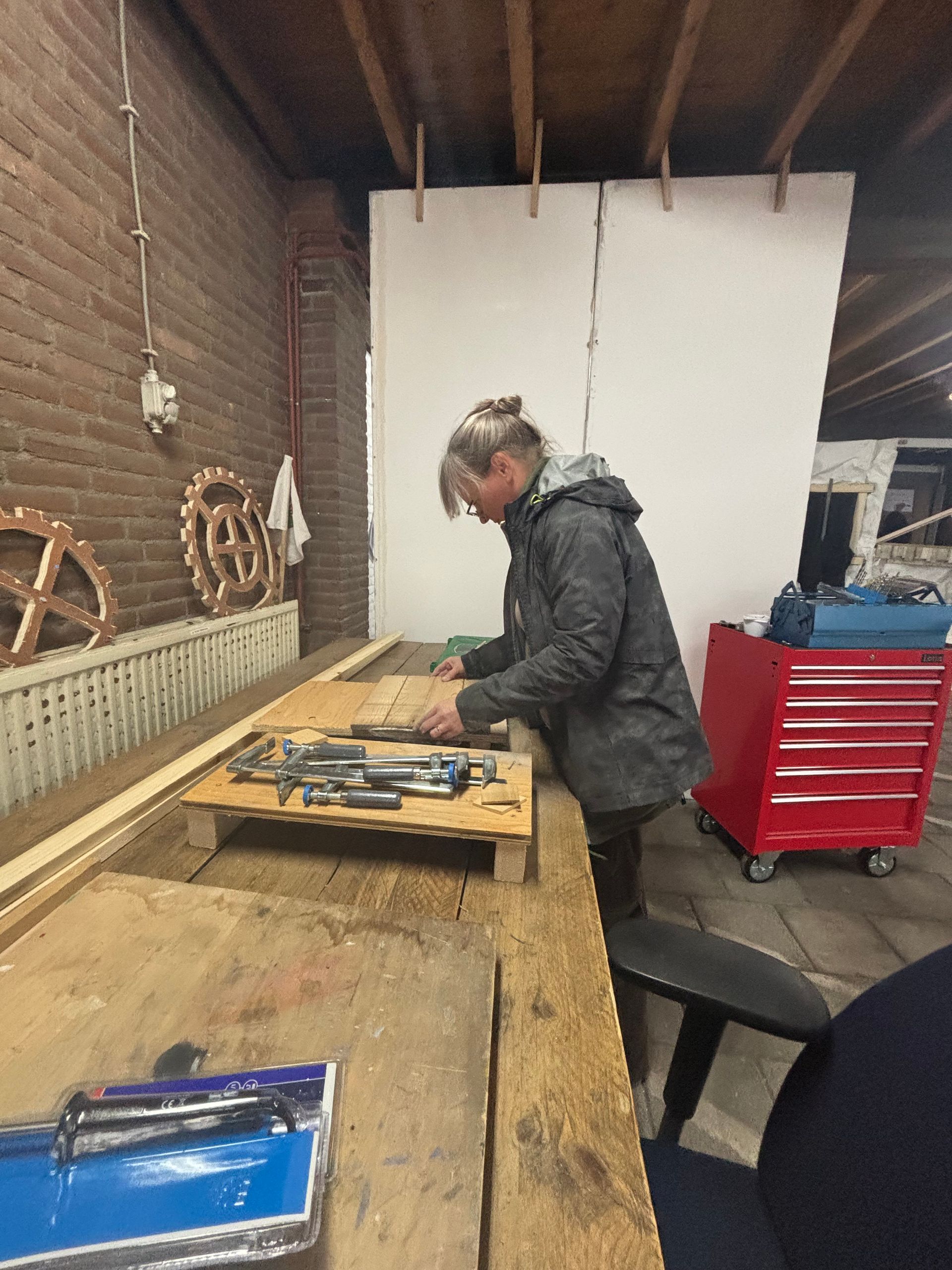 Vrouw aan het werk aan een werkbank in een werkplaats, gereedschap selecterend van een houten dienblad.