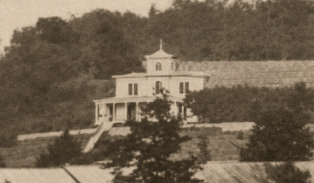 Sepia-toned building on a hillside with trees in the background and a porch in front