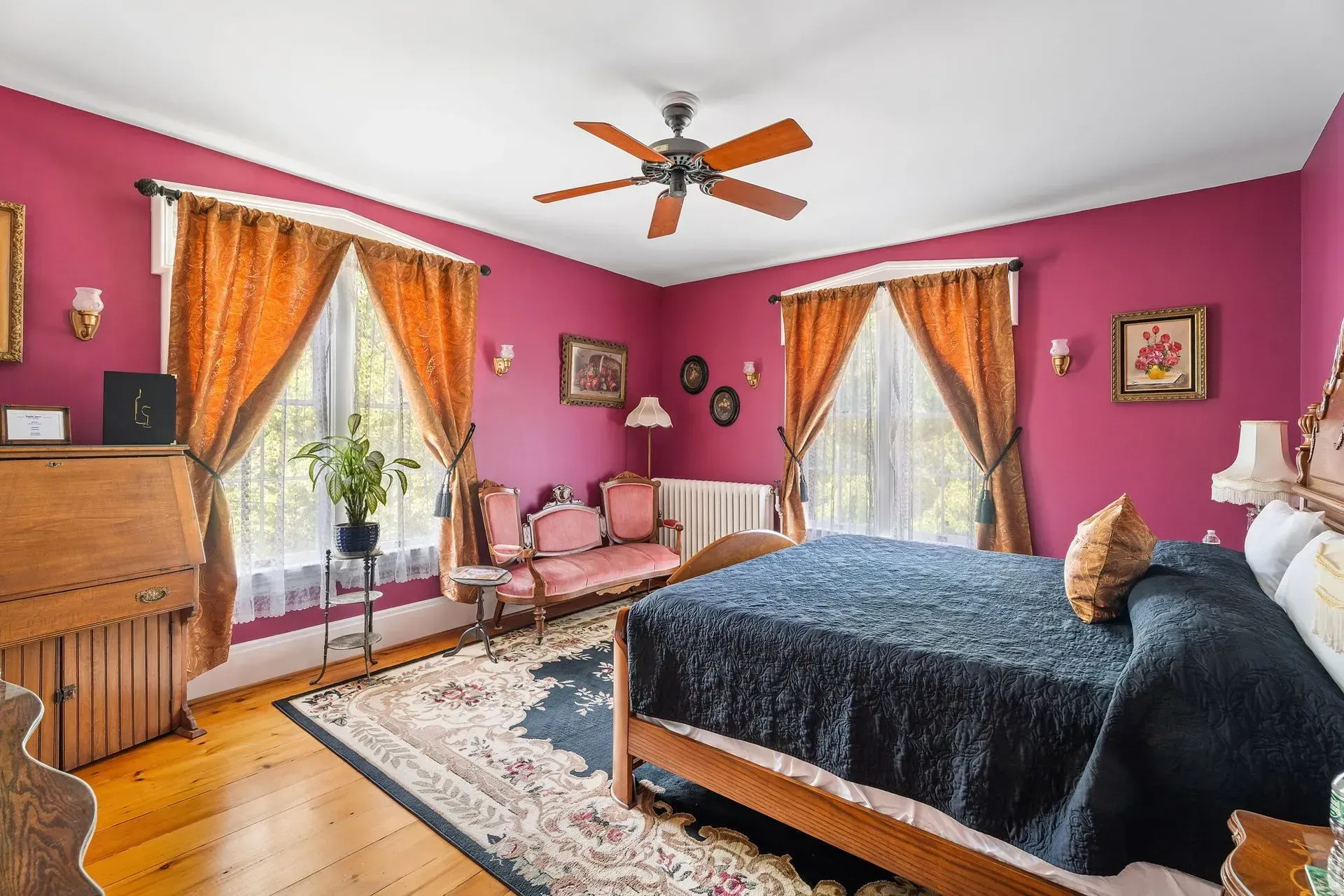 Bright pink bedroom with a bed, sofa, dresser, and orange curtains by a window