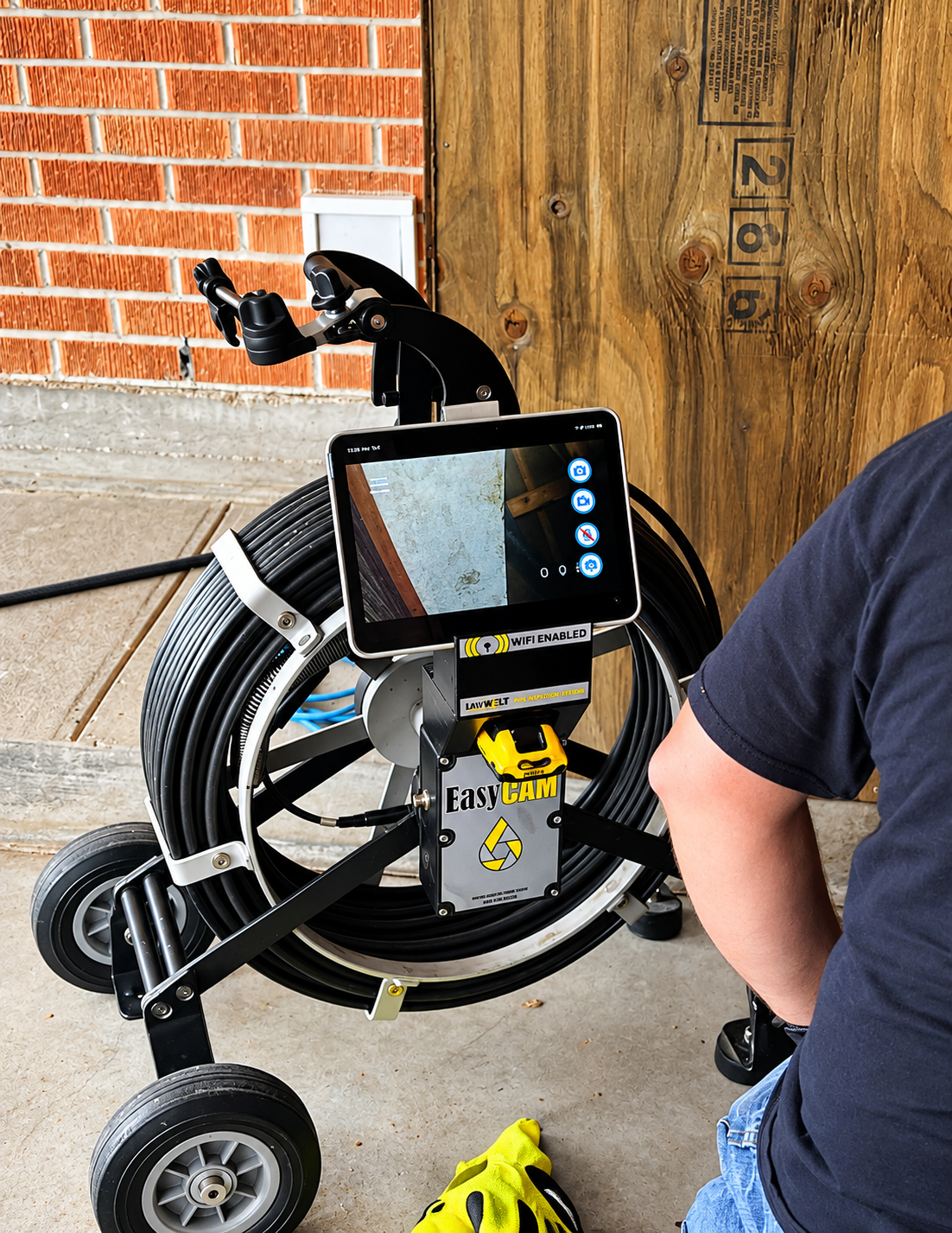 Foldable mobility scooter with a mounted tablet on a porch beside a brick wall and wooden door.