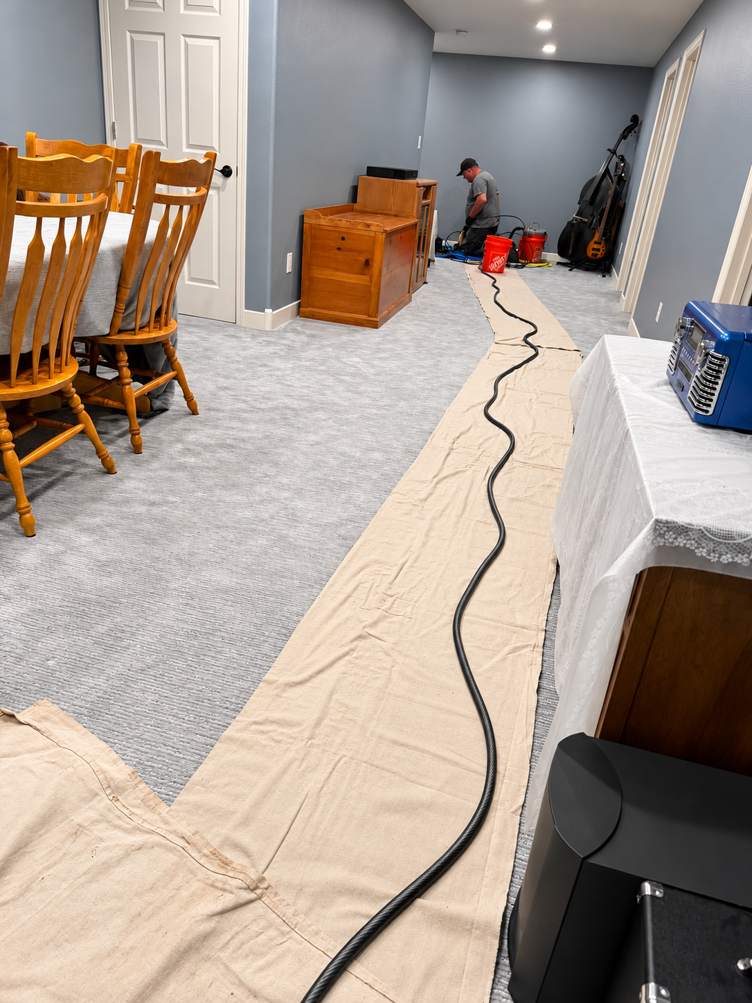 Worker in a yellow hard hat installs floor vent in a room with hardwood flooring.