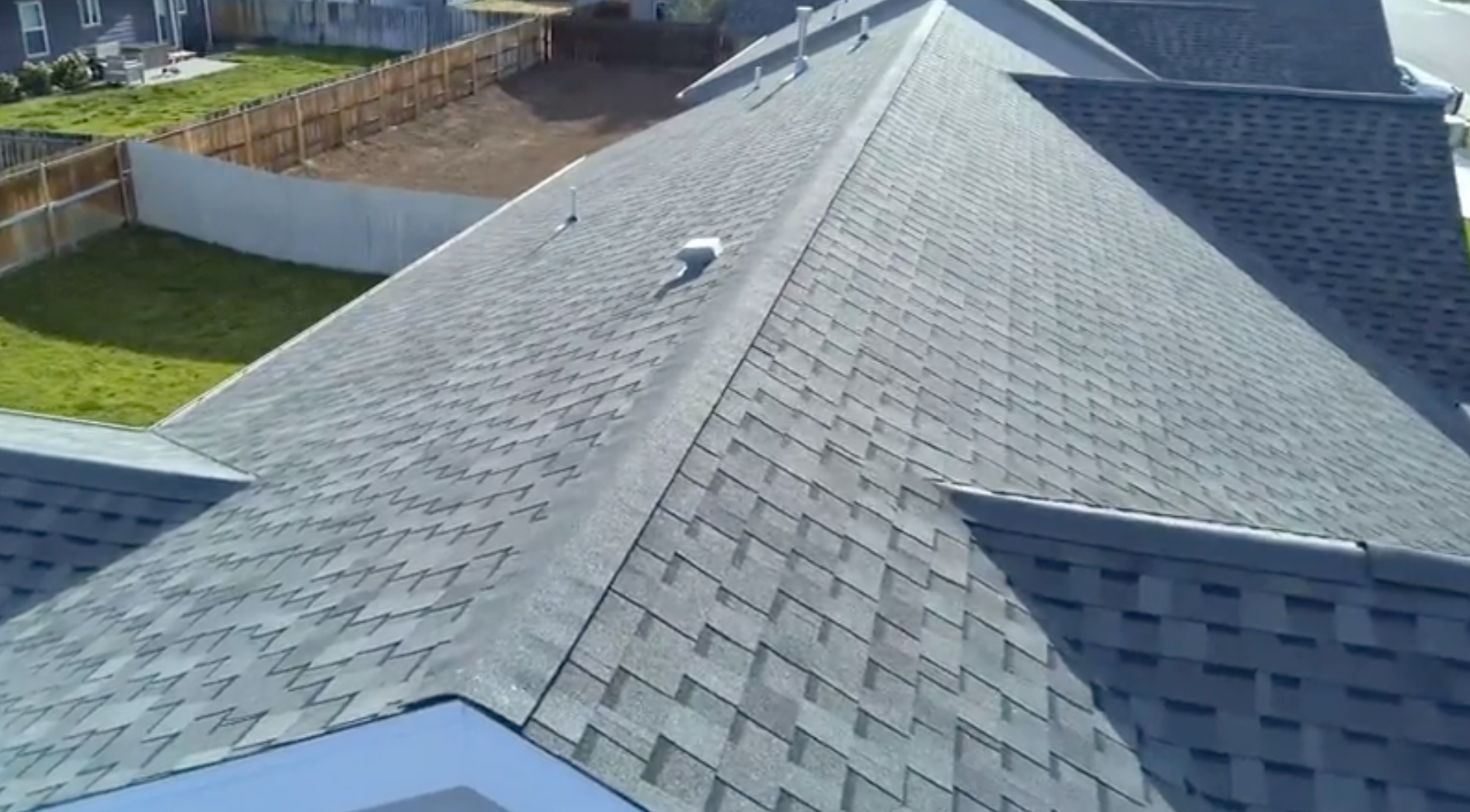 Aerial view of a gray shingled roof with multiple slopes and a small blue-roofed section