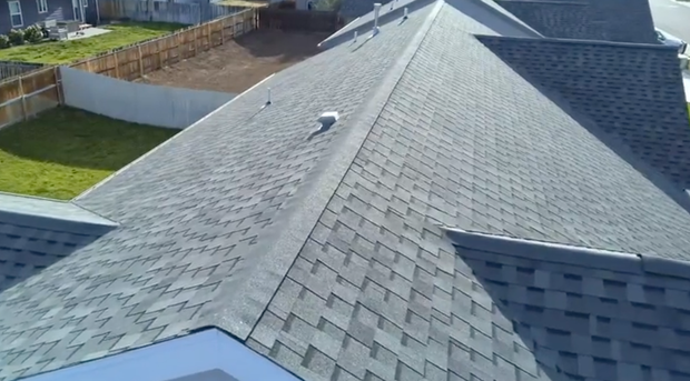 Shingled residential roof viewed from above, with a small lawn and neighboring houses in the background