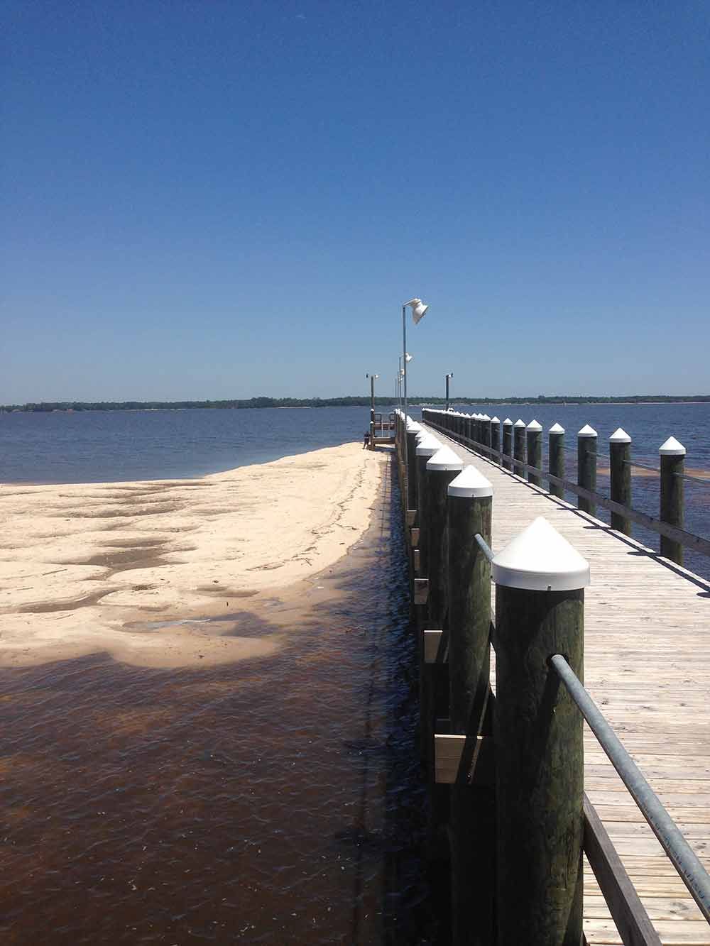 A long wooden pier leading to a sandy beach