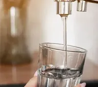 Water pours from a metallic kitchen faucet into a clear glass held by a hand.