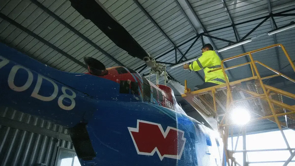 Een man werkt aan een helikopter in een hangar.