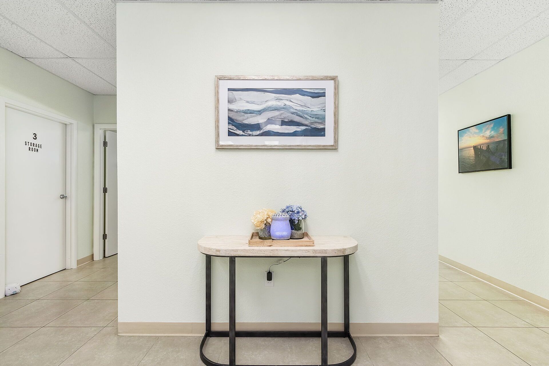 Minimal hallway with white walls, a small table, and framed wall art in a bright office space.