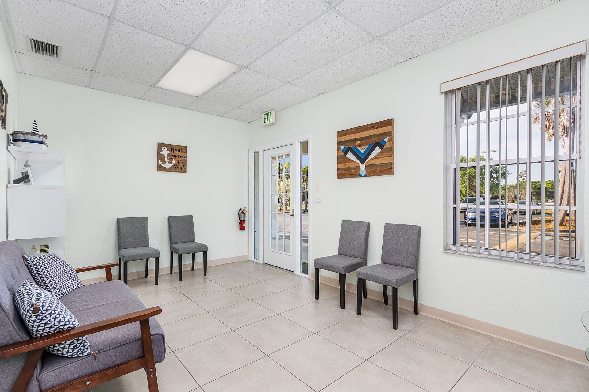 Bright waiting room with gray chairs, tiled floor, large window, and glass doors.