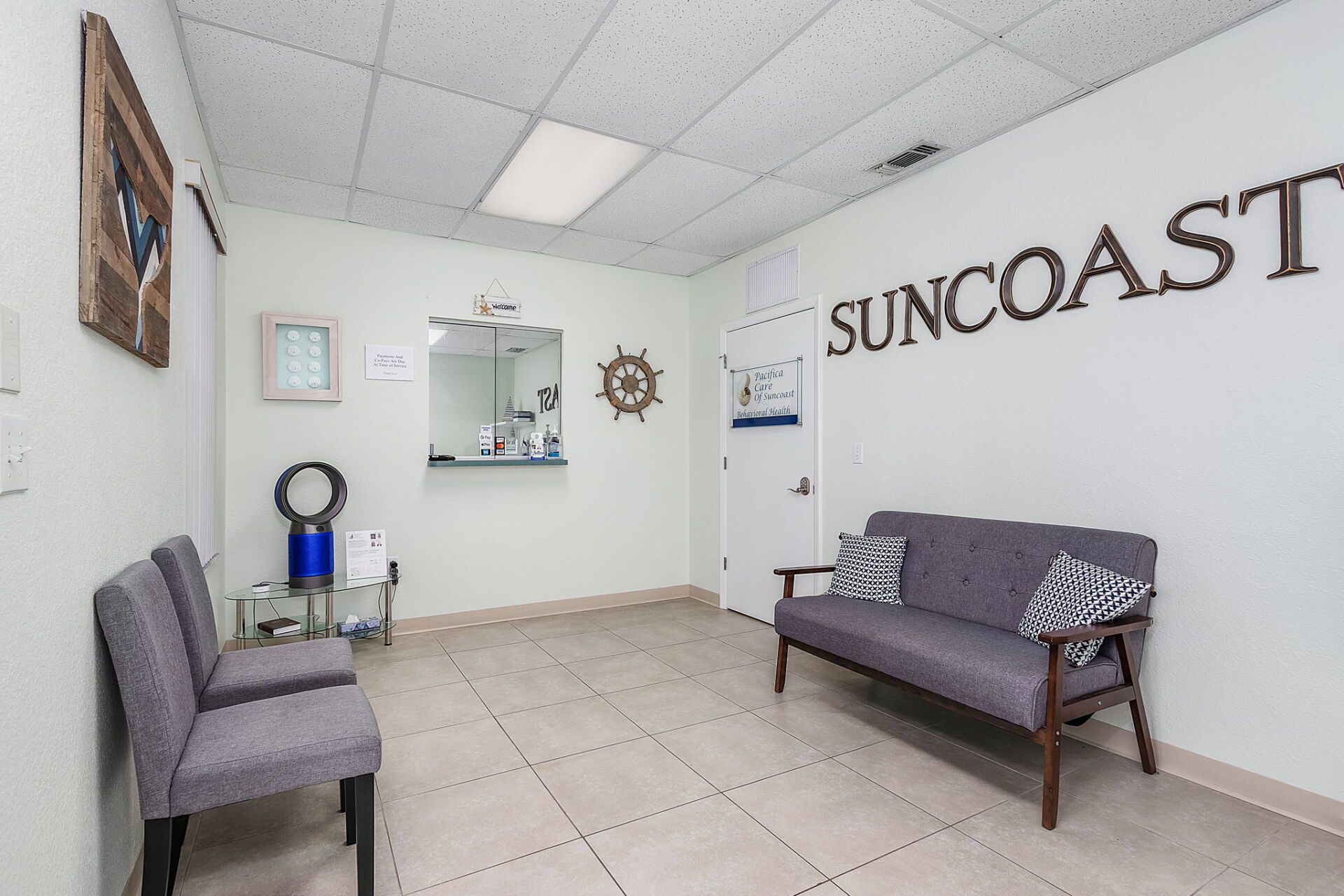 Bright waiting room with gray chairs, tiled floor, and “SUNCOAST” on the wall